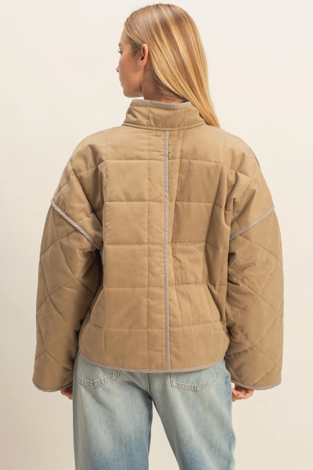 Person wearing a beige quilted jacket and light blue jeans on a plain background