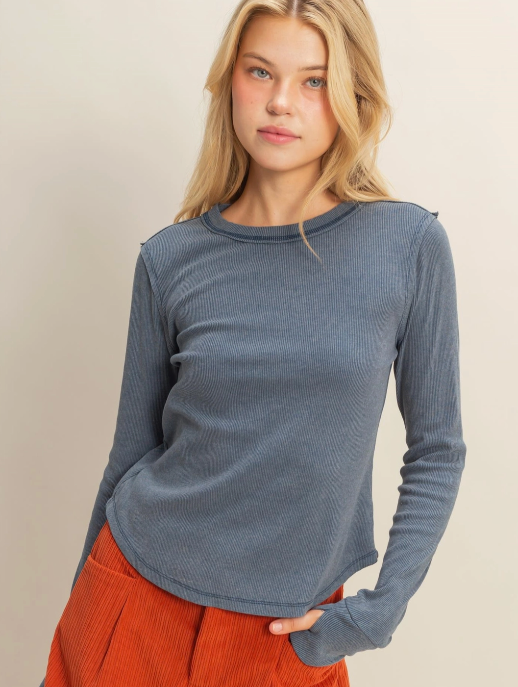Woman wearing a blue long-sleeve top and orange pants against a beige background