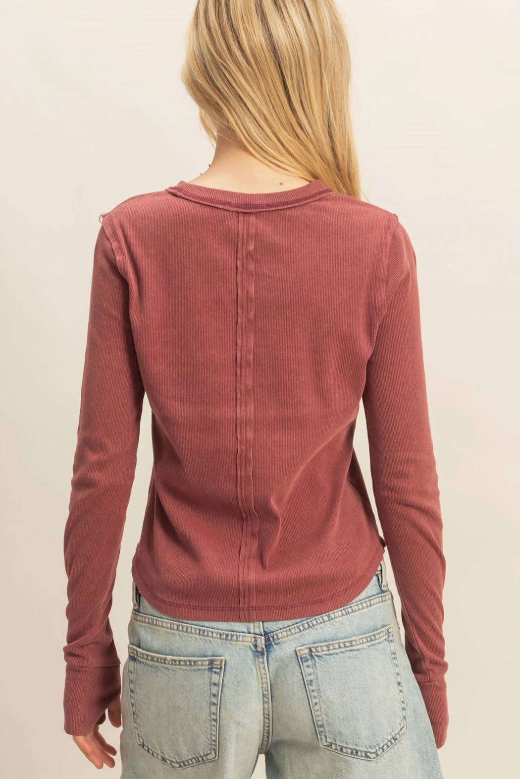 Person wearing a rust-colored long-sleeve top and light blue jeans on a beige background