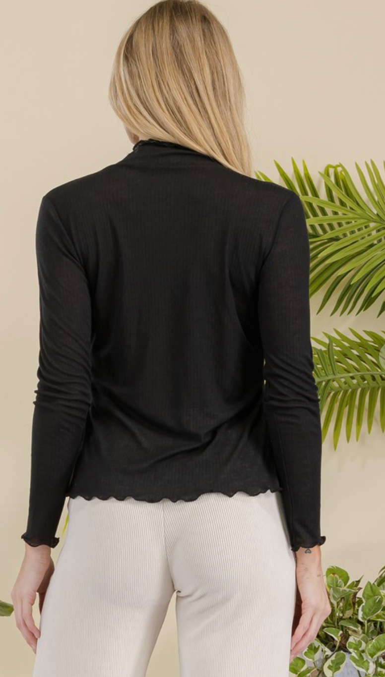 Woman wearing a black long-sleeve top with scalloped hem against a natural background