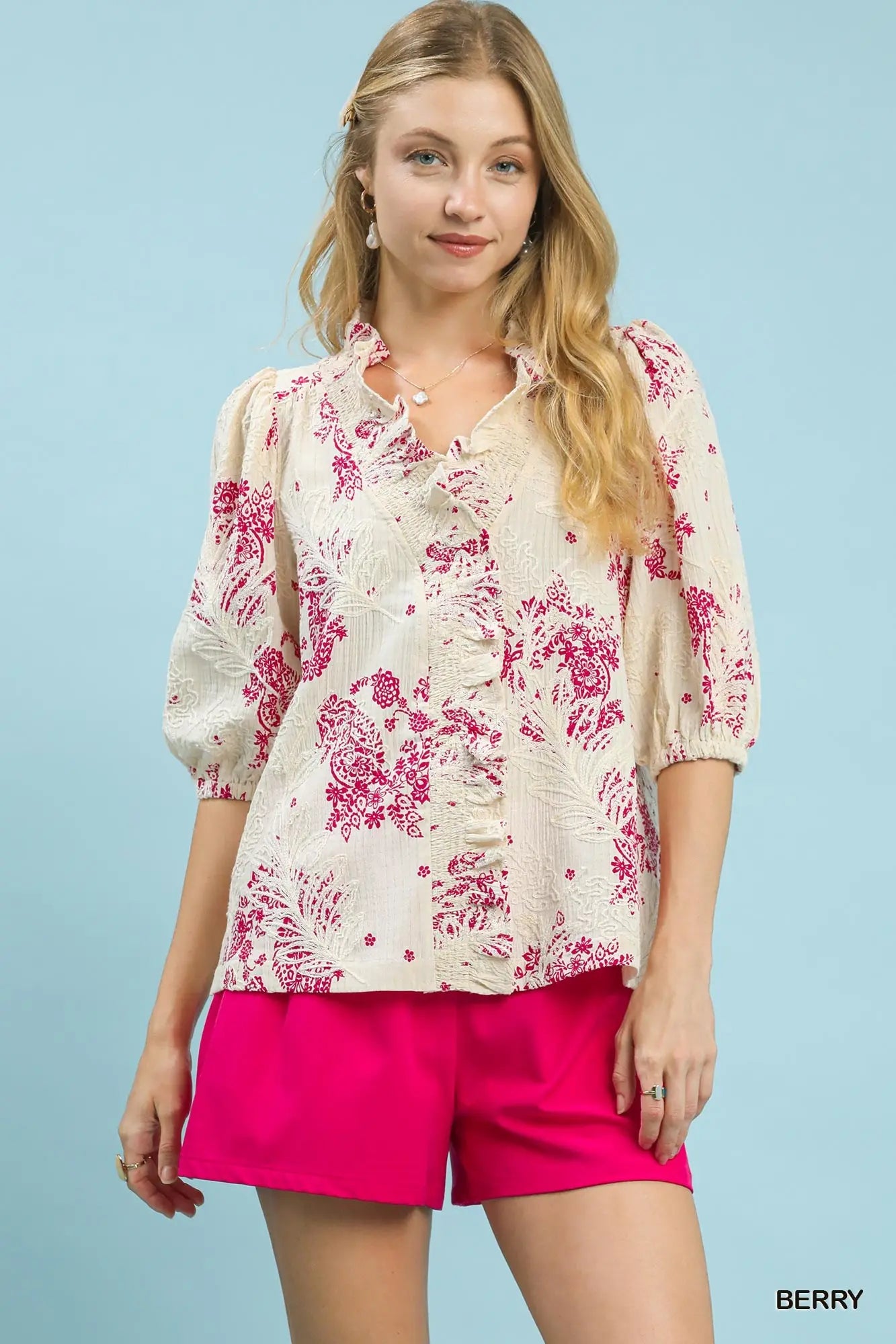 Woman wearing a floral blouse and pink shorts against a light blue background