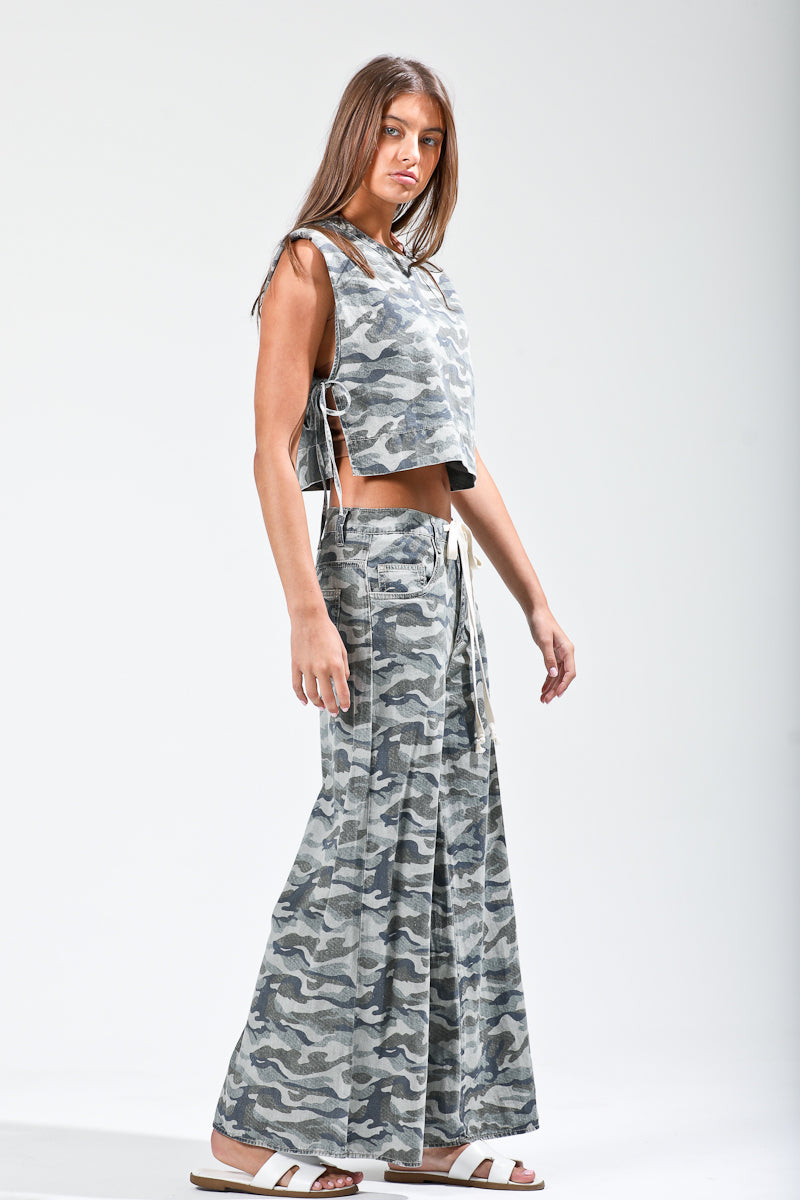 Woman wearing a camouflage outfit with a sleeveless top and long pants on a white background