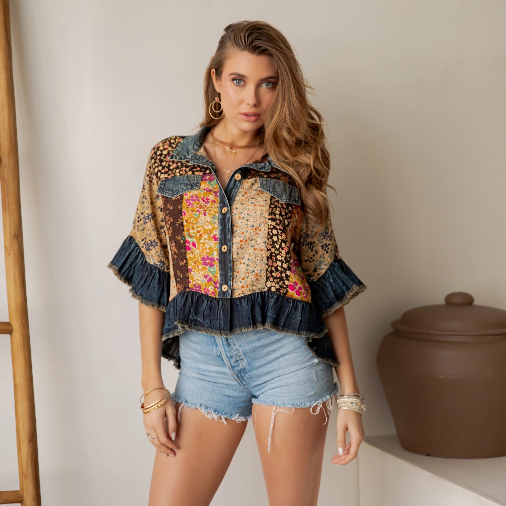 Woman wearing a patterned shirt and denim shorts standing against a neutral background