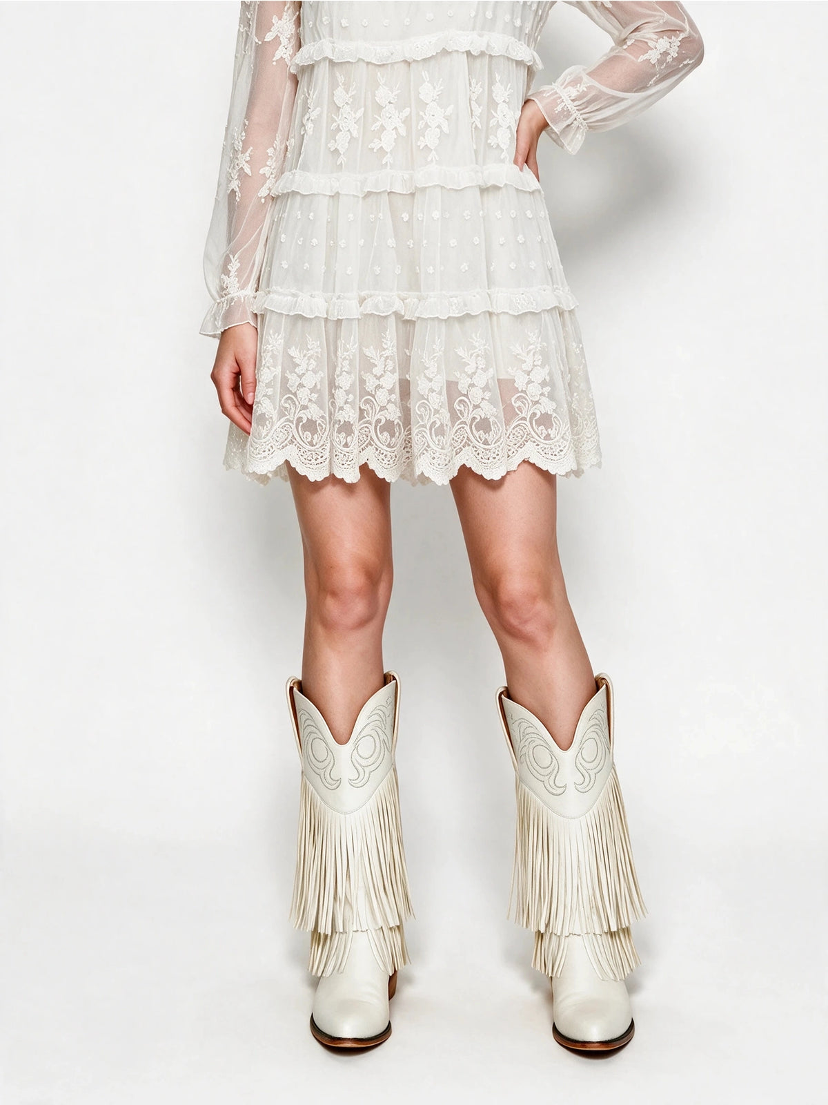 Close-up of the white tiered skirt and scalloped embroidered lace hem, paired with ivory fringe cowboy boots.