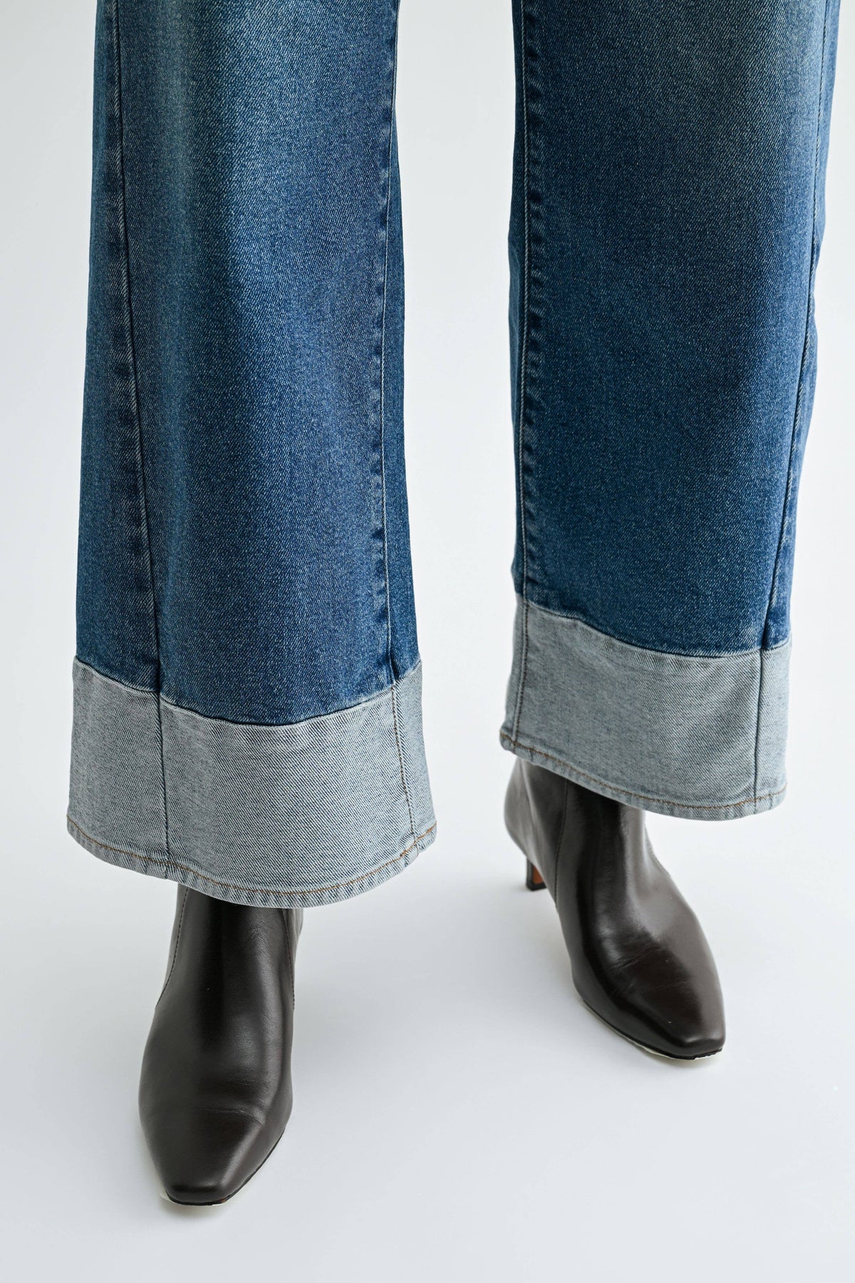 Close-up of Blue Hour jeans showing vertical leg seams and two-tone light denim hems above black pointed-toe ankle boots.