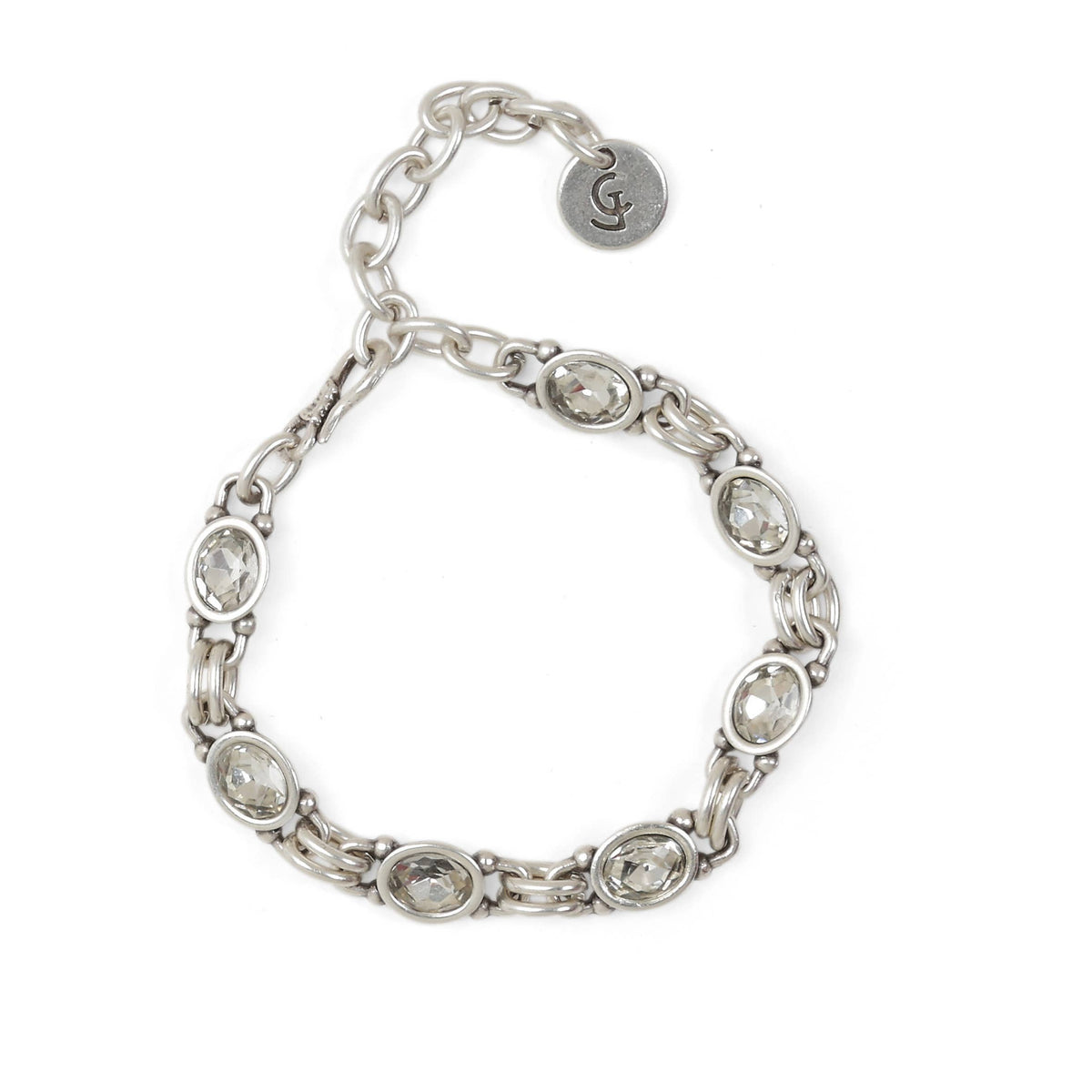 A silver-toned chain bracelet with oval clear gemstones set in polished metal, featuring a lobster clasp and an adjustable round tag with an engraved monogram.