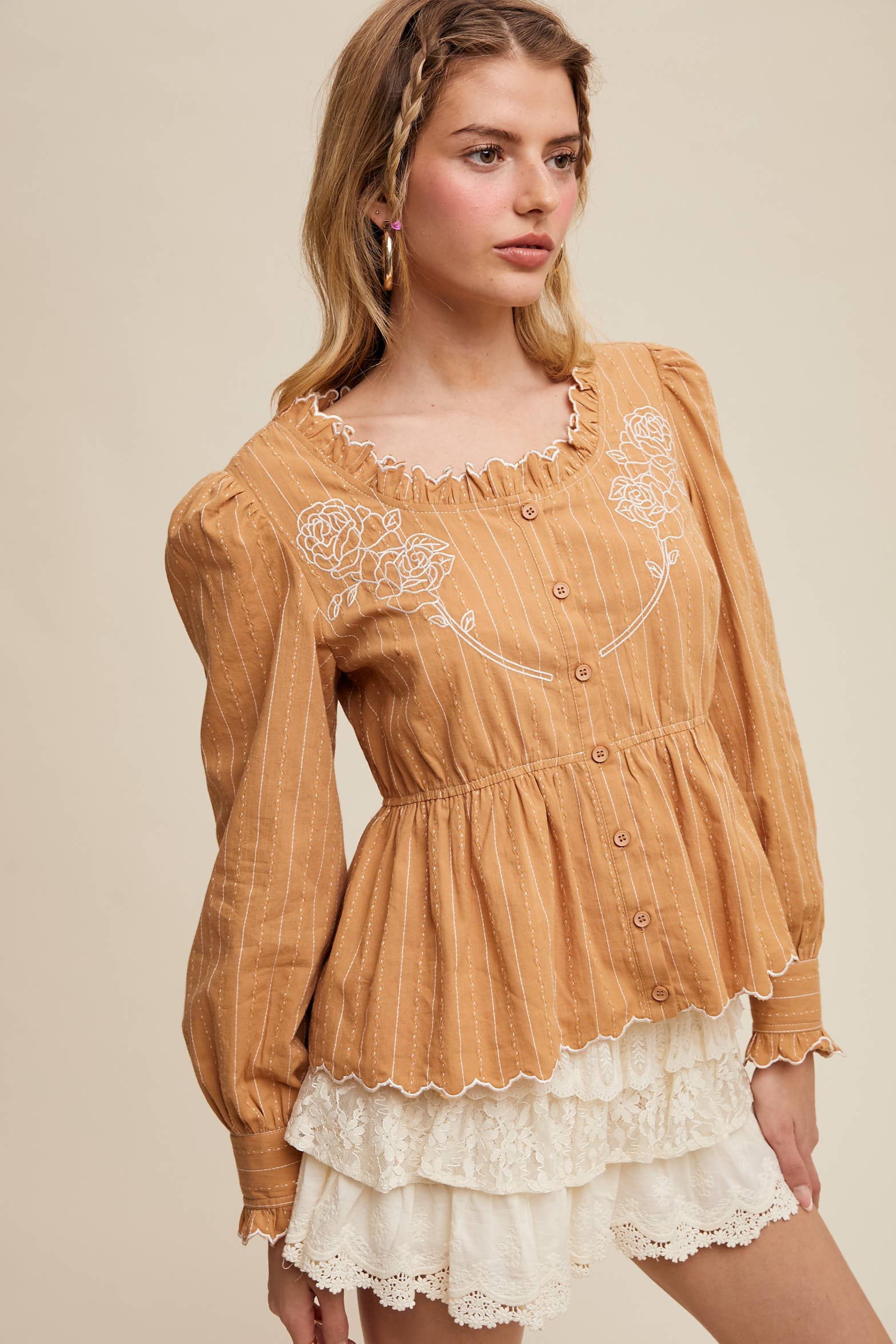Camel pinstripe blouse with ruffled neckline, white rose embroidery, puff long sleeves, button front, and scalloped peplum hem—styled with white lace shorts.