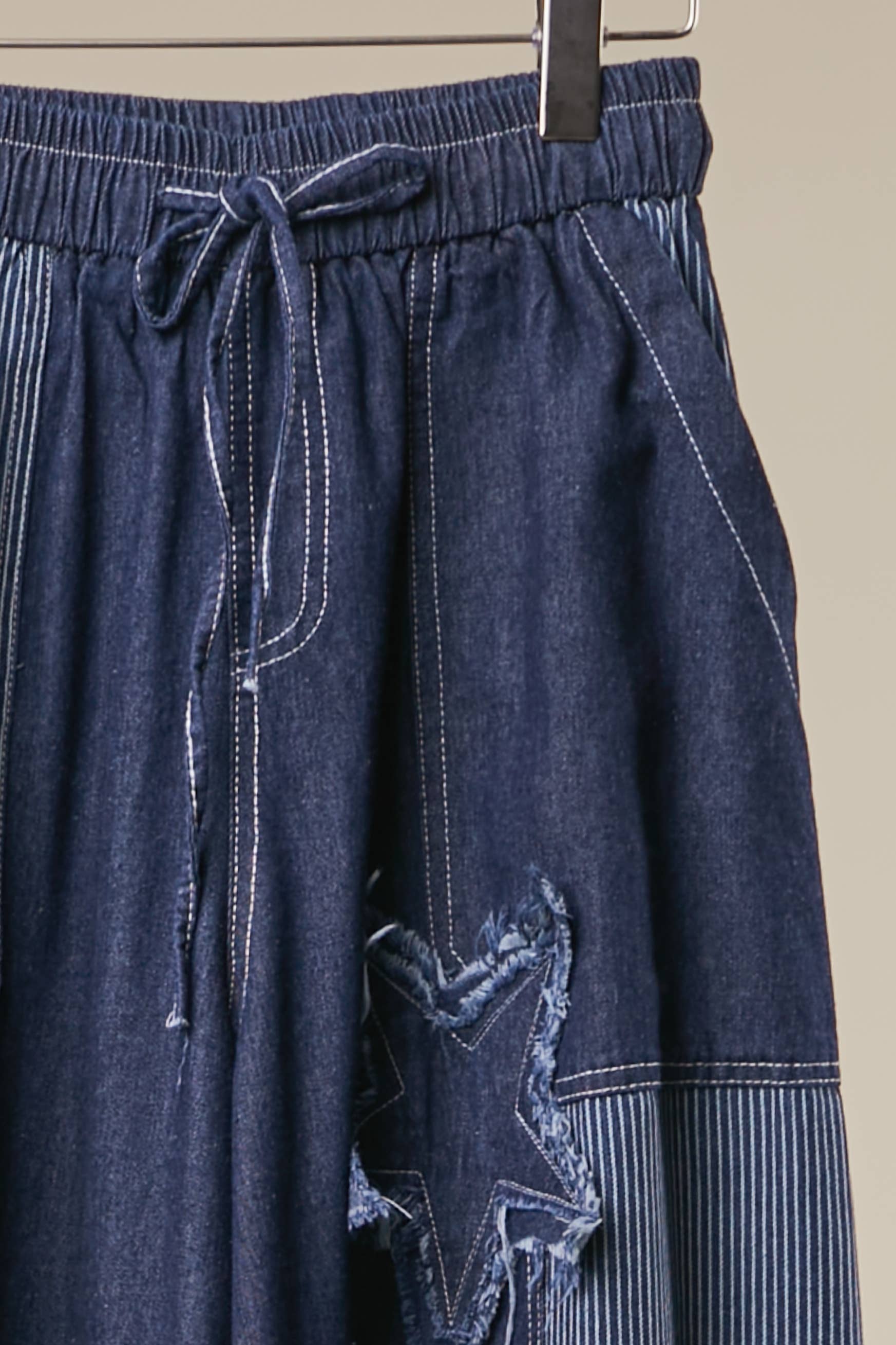 close up of Blue Star Wide Leg Patchwork Denim Pants in dark blue wash with frayed star patches, elastic waist and drawstring — boho wide leg style by Mello