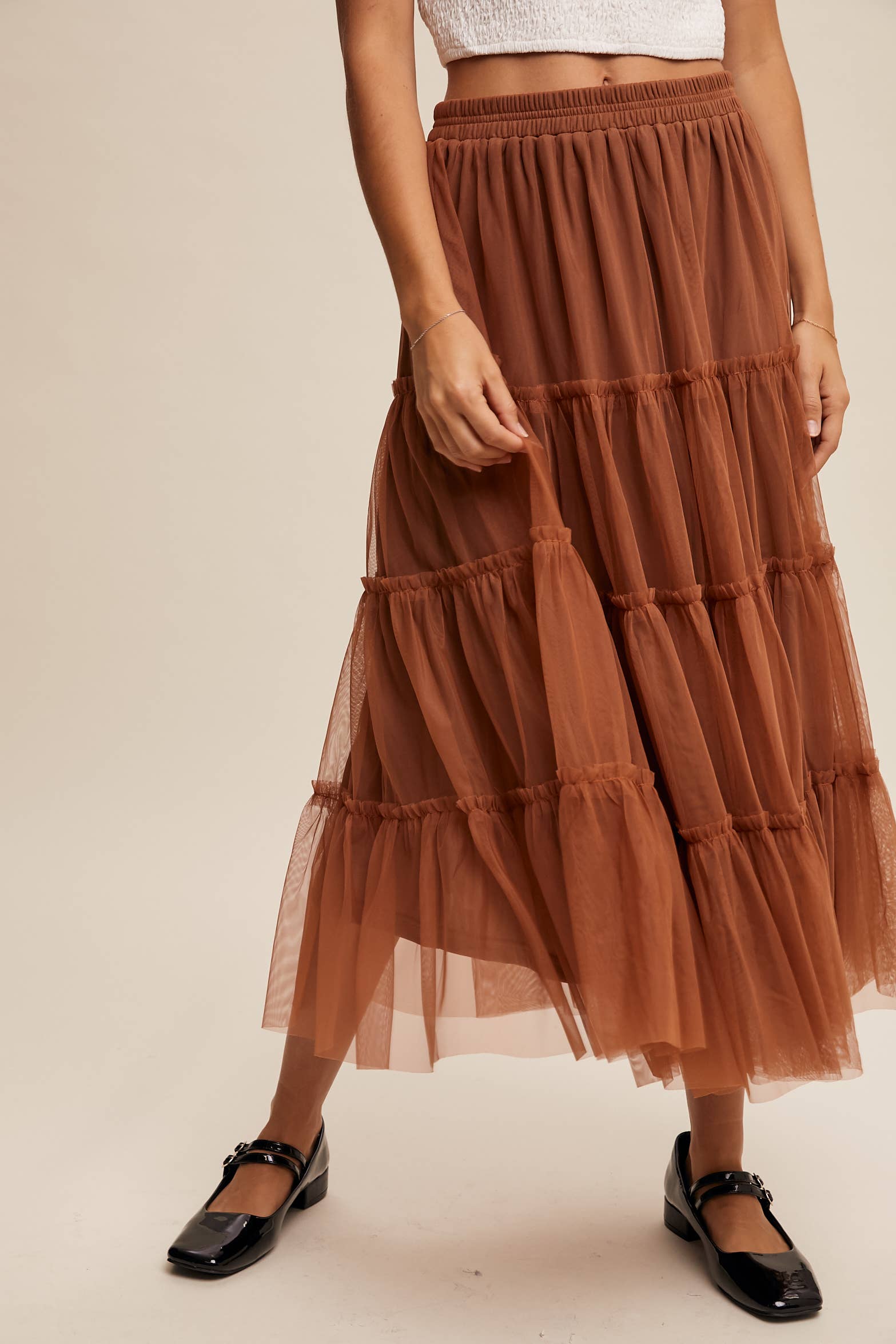 Close-up — rust tulle tiered midi skirt with elastic waist and ruffled layers, sheer overlay, styled with black Mary Jane flats.
