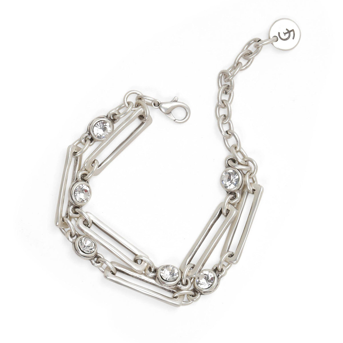 A silver-toned chain bracelet with multiple linked bar elements and clear round gemstones, shown on a plain white background. A small round tag with an Om symbol is attached to the chain.