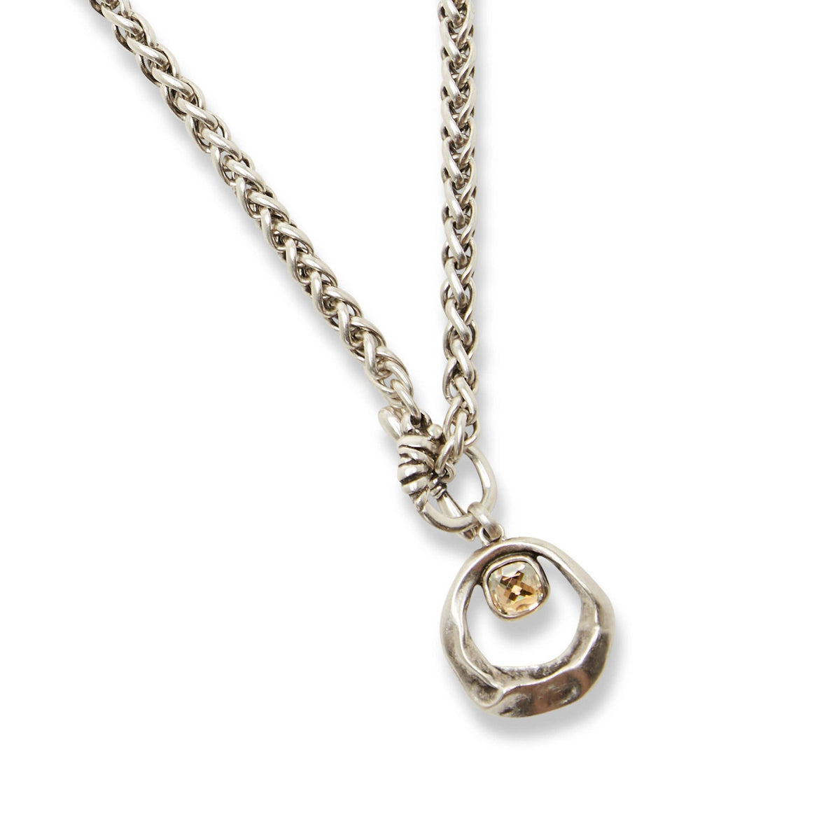 A silver-toned chain necklace with a textured circular pendant featuring a small, bezel-set yellow gemstone, shown on a clean white background.