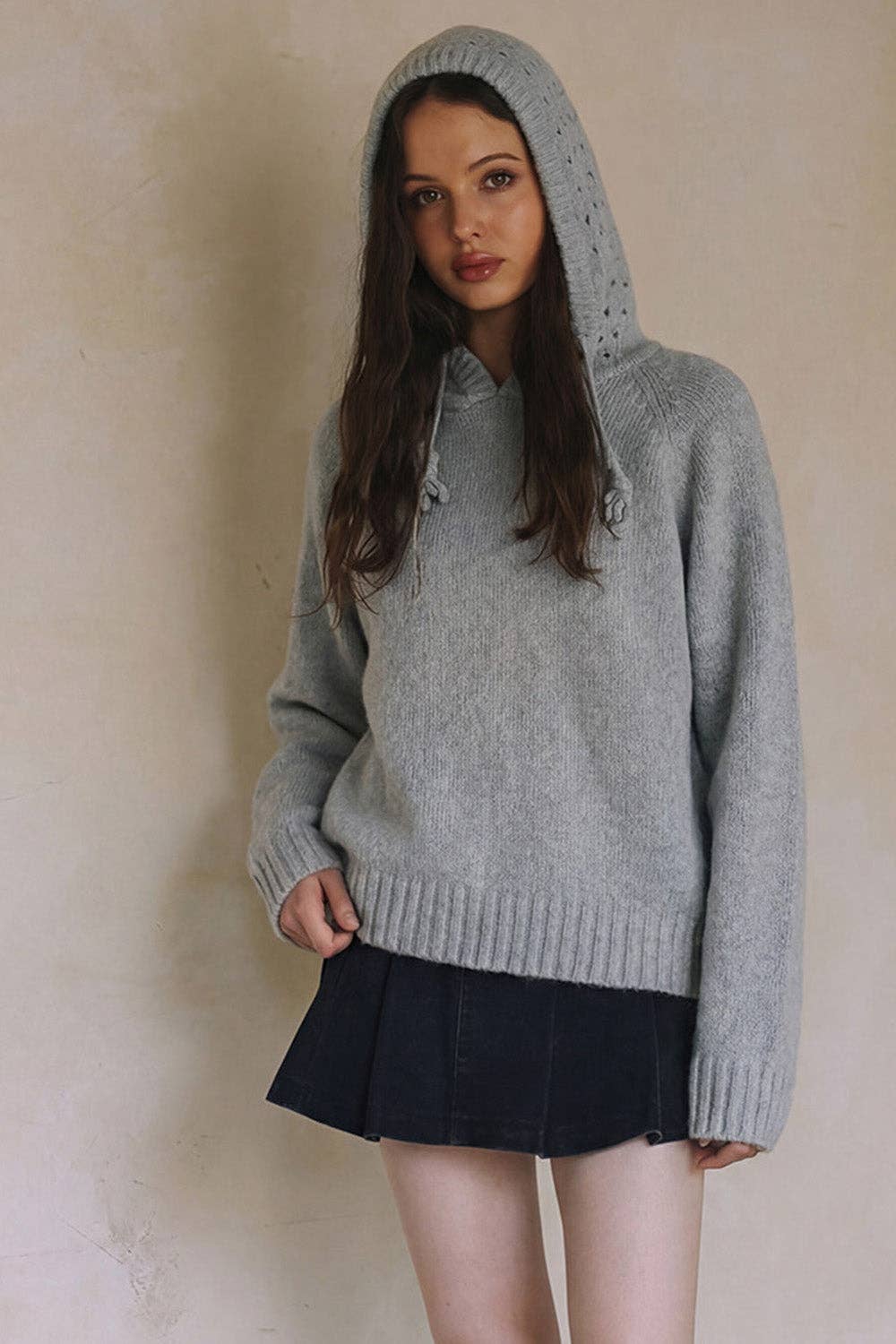 Woman wearing a gray hooded sweater against a beige background