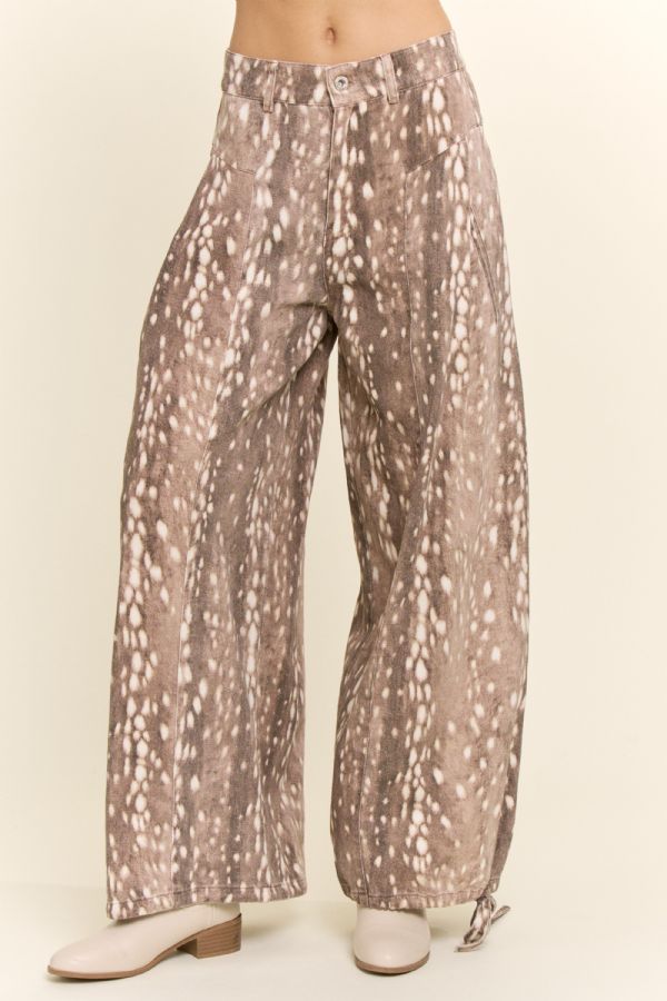 A person wearing wide-leg pants with an abstract spotted print in taupe, beige, and white, paired with light beige heeled shoes against a plain cream studio background.