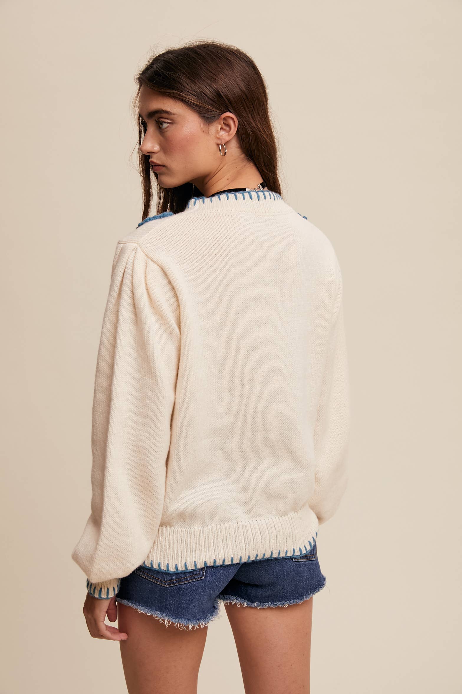 Back view- Side view- Cream sweater with blue crochet flower appliqués at neckline, blue whipstitch trim at cuffs and hem, long sleeves; styled with frayed denim shorts.