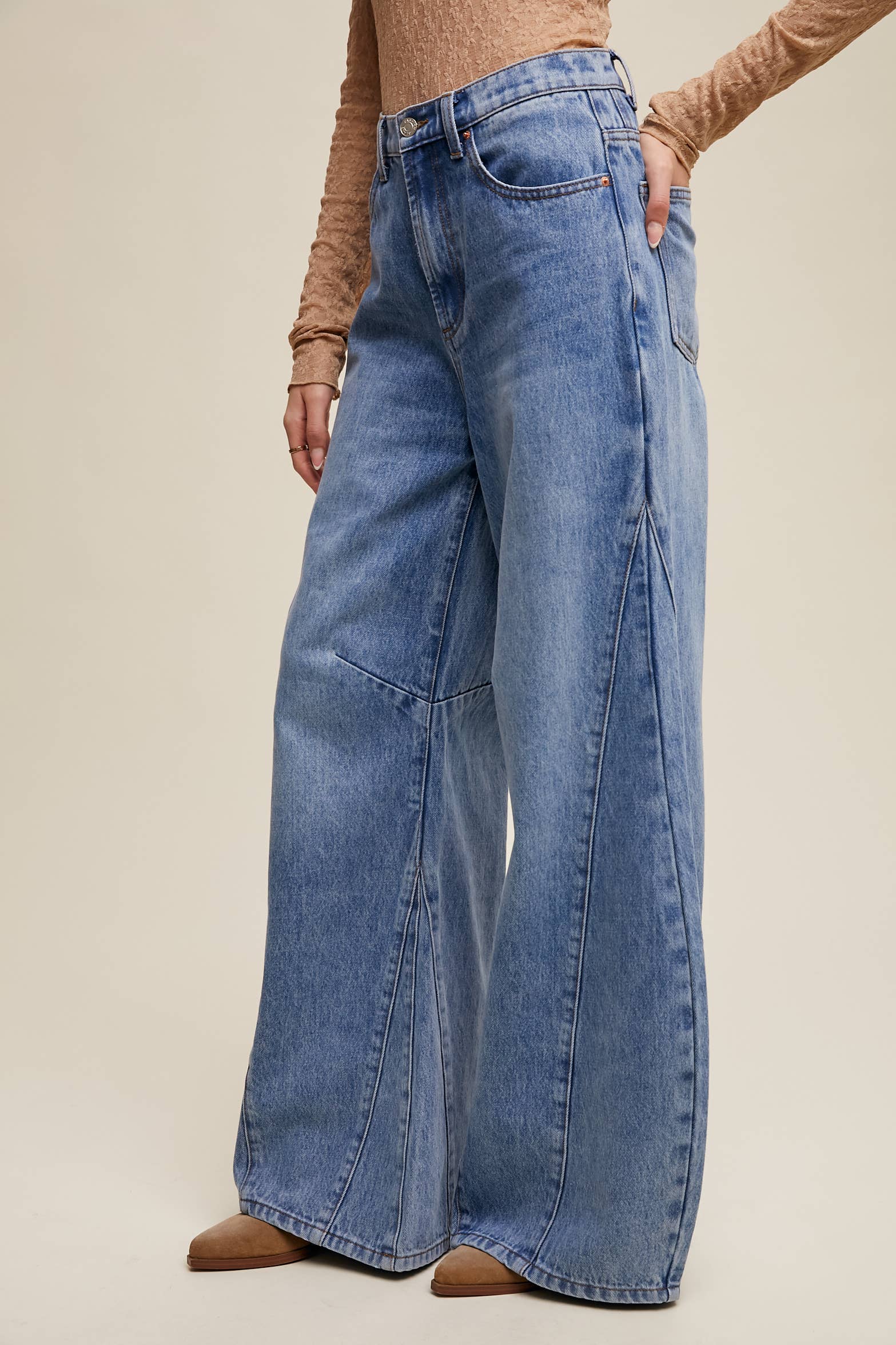 Side view- High-rise light-wash wide-leg jeans with front seam panels and knee darts, five-pocket style with zip fly, styled with tan long-sleeve top and pointed-toe boots.