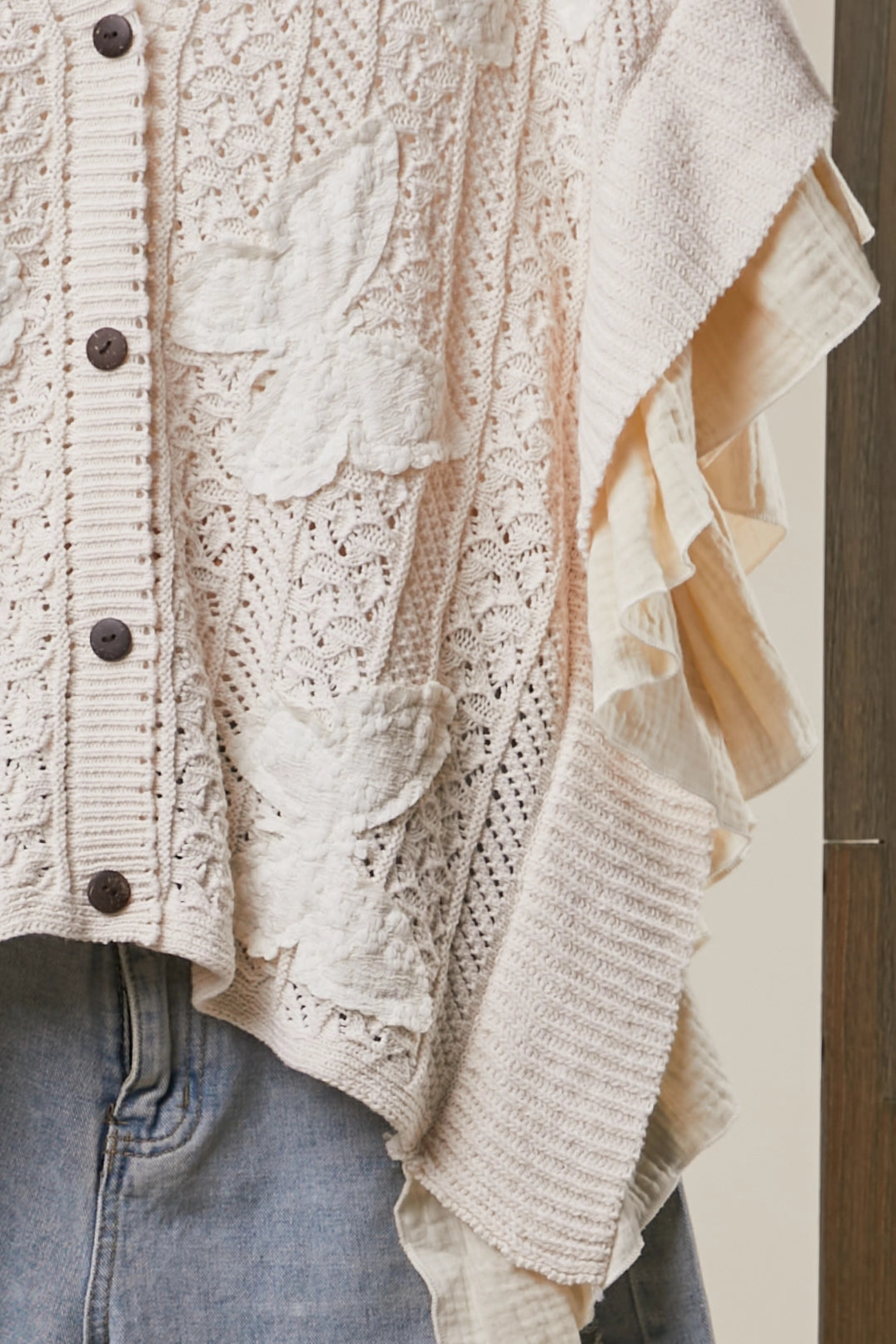 Close-up of Butterfly Bloom Cardigan cream-colored lace and knit cardigan with ruffled trim, shown worn over light blue jeans.