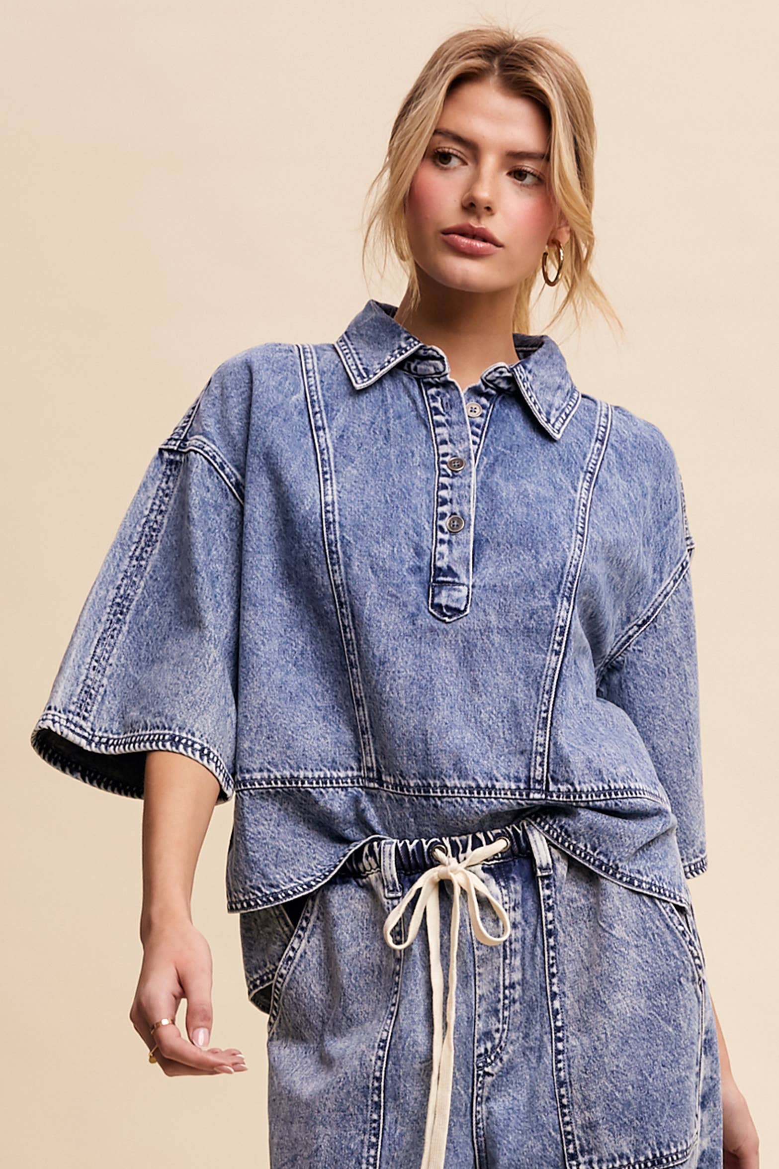 Light-wash denim pullover top with a half-button placket, exposed seam panels, and wide elbow-length sleeves in a relaxed, boxy fit.