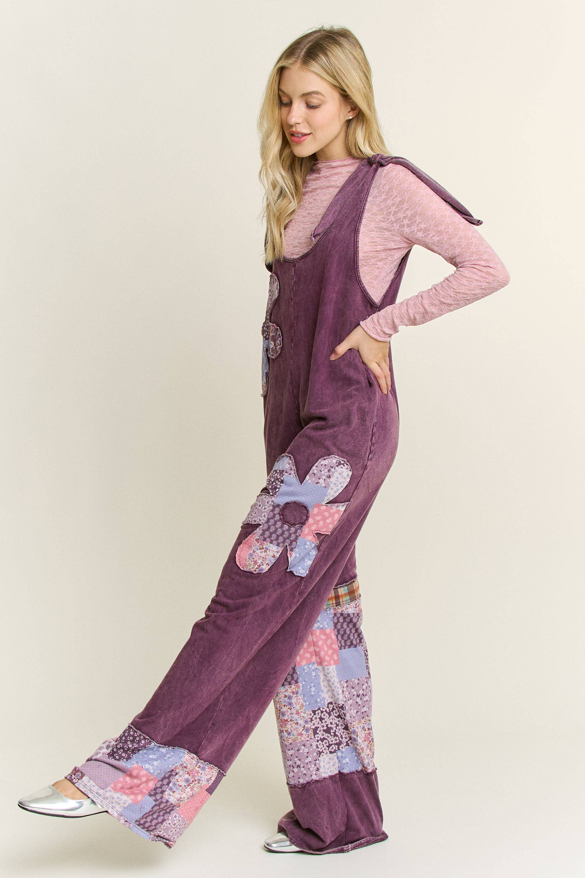 Side view of Woman wearing boho patchwork mineral-wash jumpsuit with daisy appliqués and wide legs.