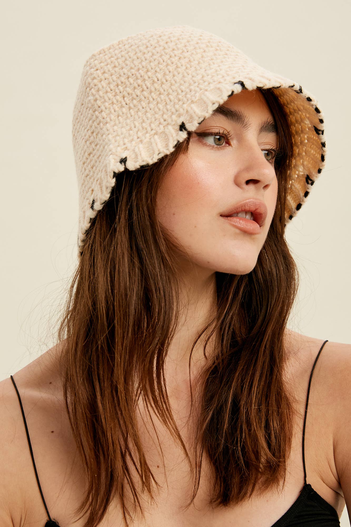 Close-up — cream knit bucket hat with contrast black whipstitch edging and soft brim, on model.