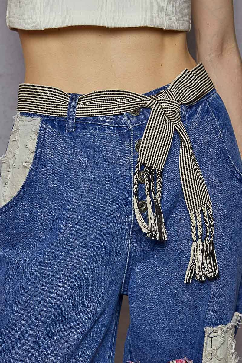 Close-up of a black and cream striped woven belt with braided fringe tassels tied at the waist of blue denim jeans.