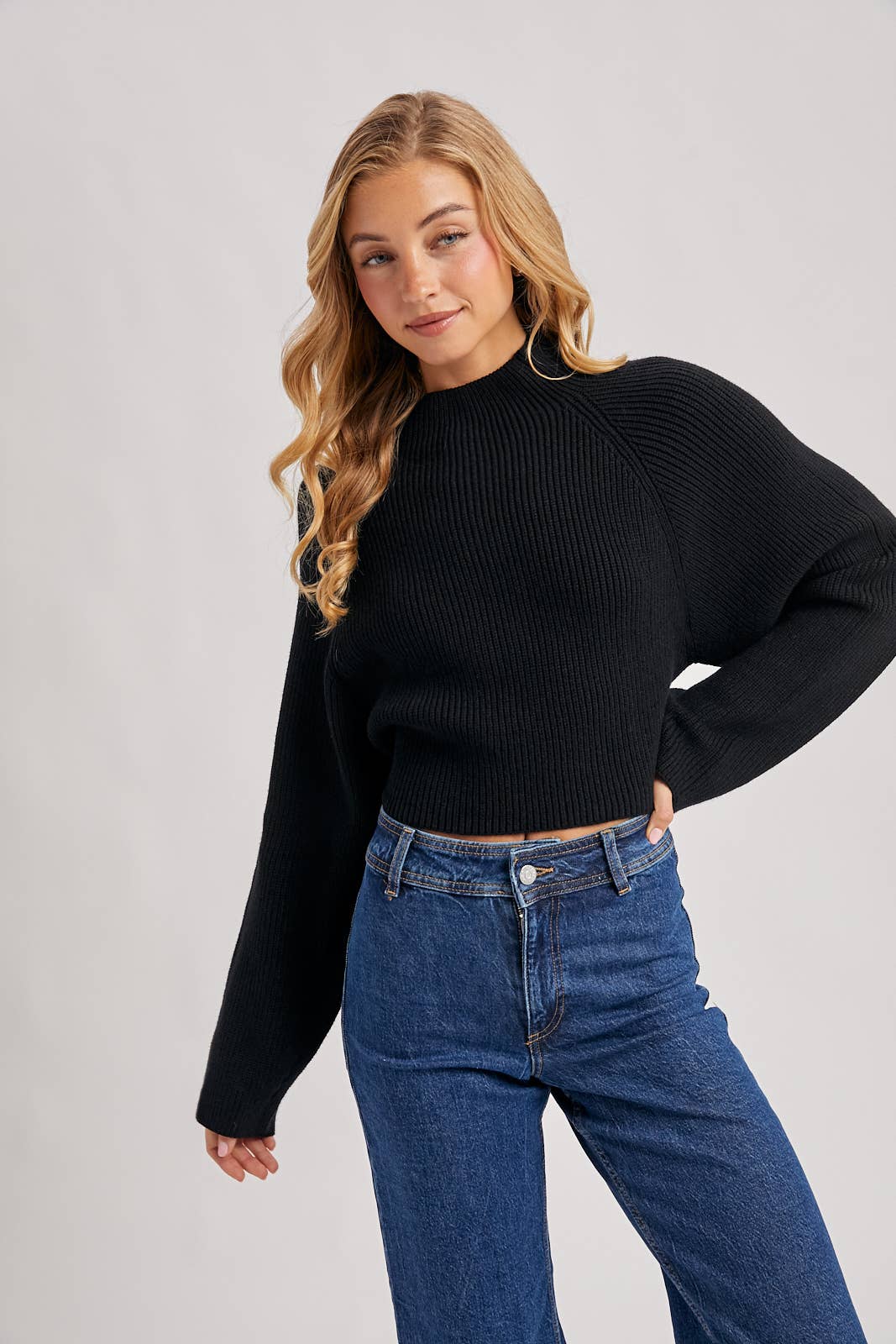Black ribbed mock-neck sweater with long wide sleeves and a cropped fit, styled with high-rise blue jeans.