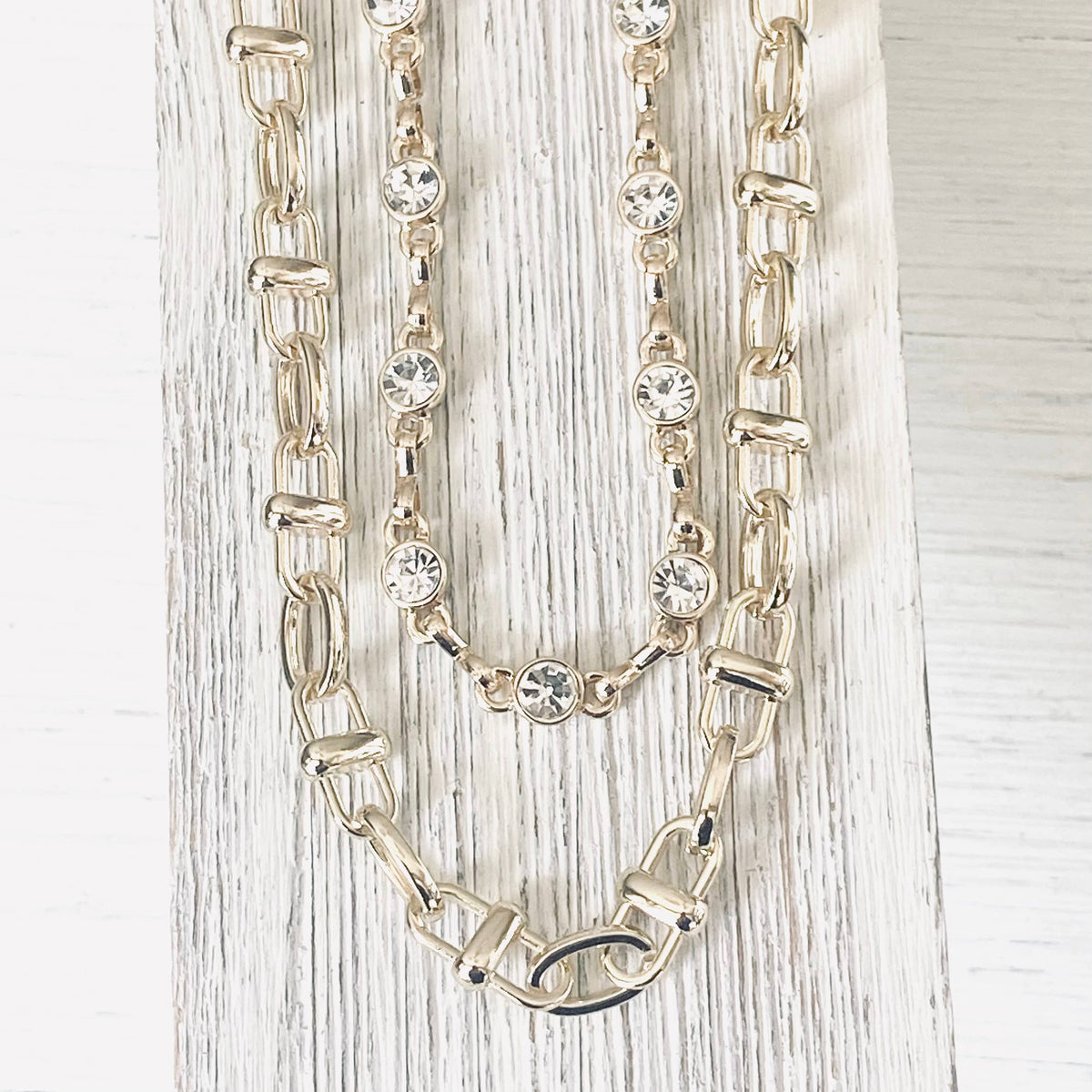 Gold chain necklace with embedded crystals on a light wooden surface