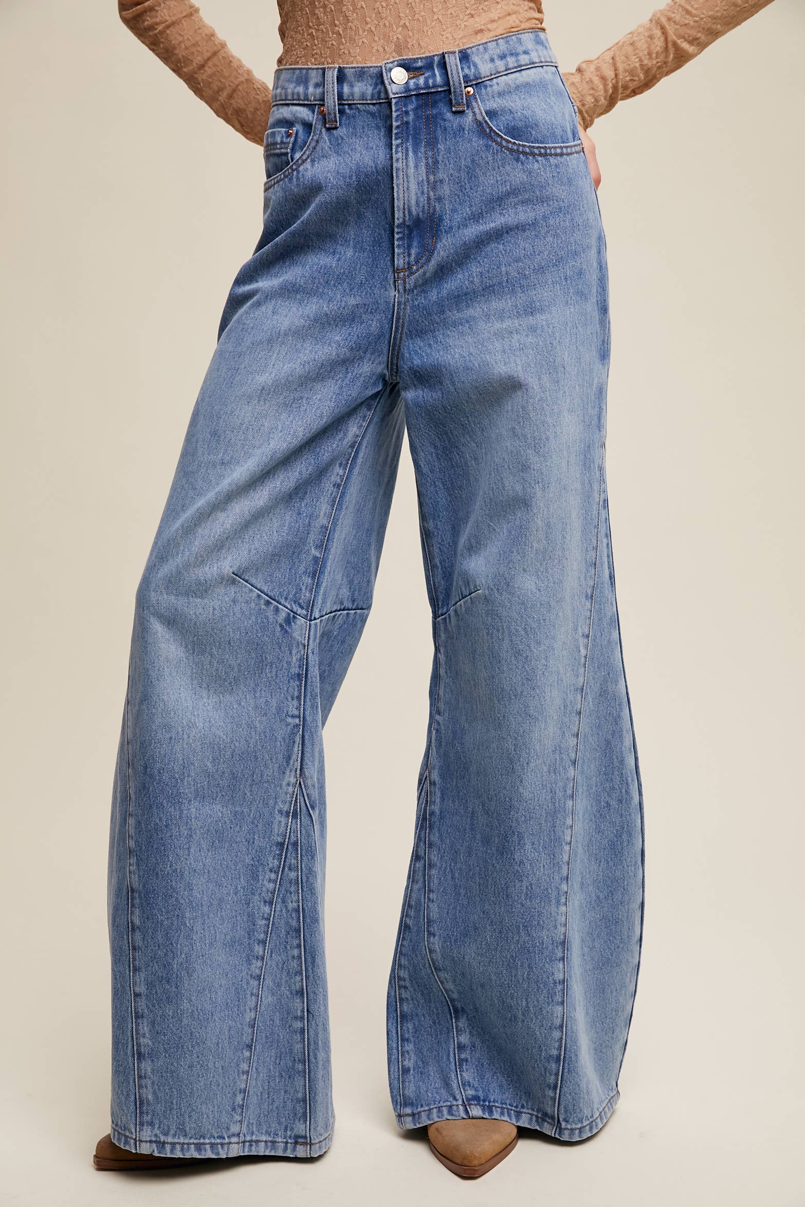 High-rise light-wash wide-leg jeans with front seam panels and knee darts, five-pocket style with zip fly, styled with tan long-sleeve top and pointed-toe boots.
