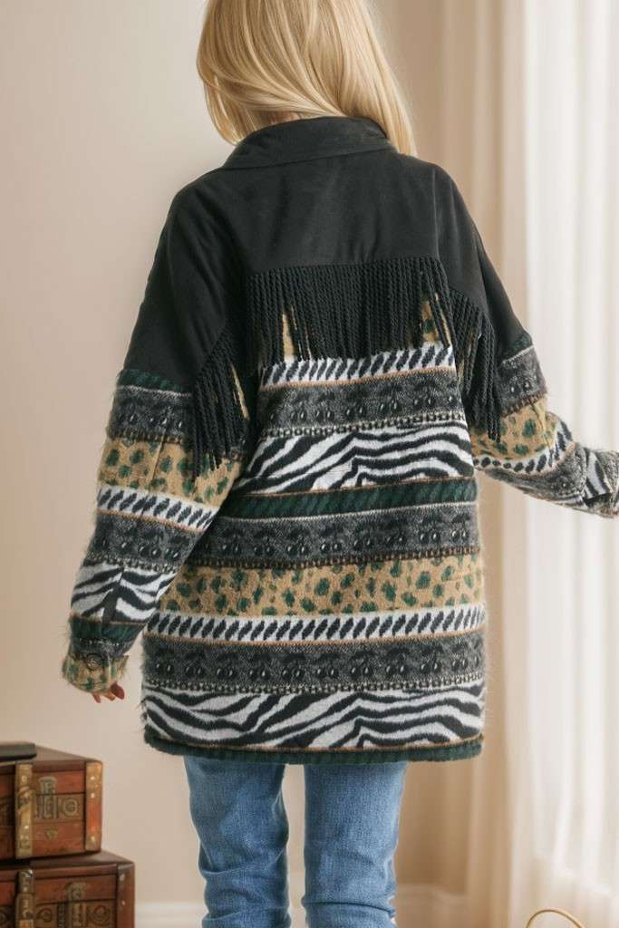 Brown Aztec print shacket with fringe detail, button closure, and patterned sleeves, styled with cream pleated pants while seated on a sofa.