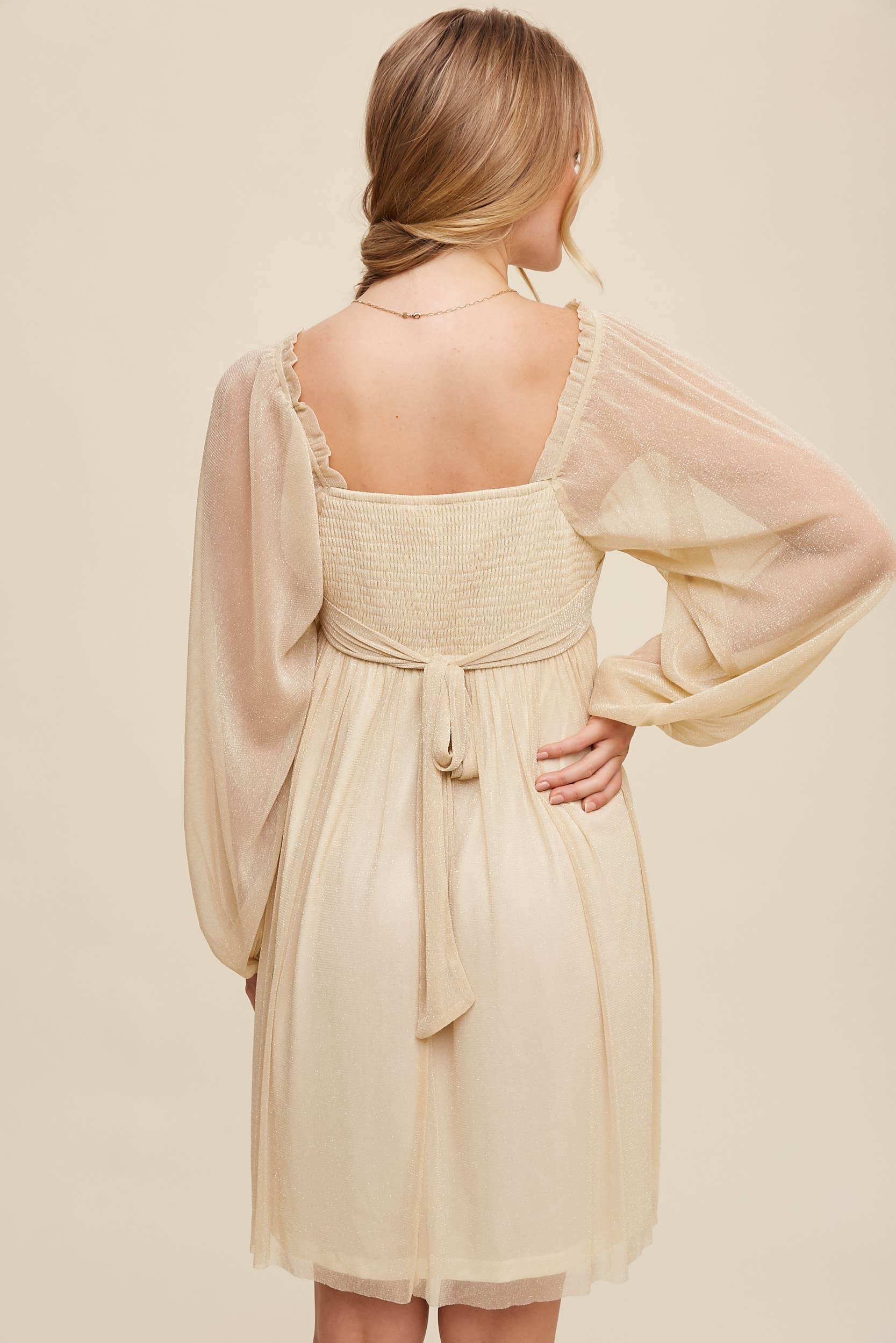 Back view Model wearing a beige shimmer mini dress with long sheer sleeves, square neckline, and flowy A-line silhouette — romantic sparkle party dress