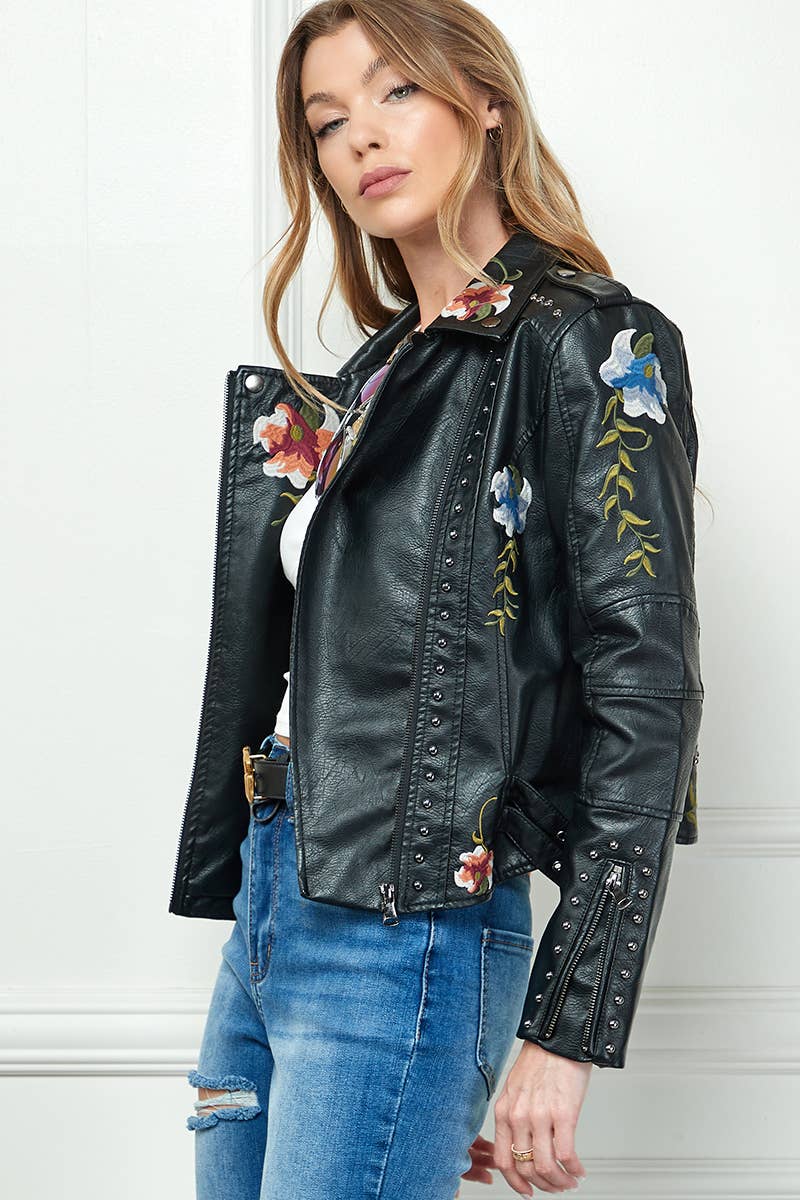 Black faux-leather moto jacket with floral embroidery and silver studs, styled with a white crop top and high-waisted blue jeans.