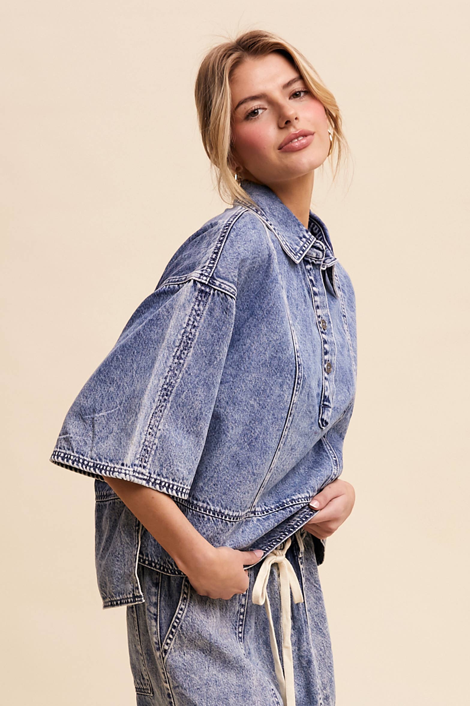 Side view- Light-wash denim pullover top with a half-button placket, exposed seam panels, and wide elbow-length sleeves in a relaxed, boxy fit.