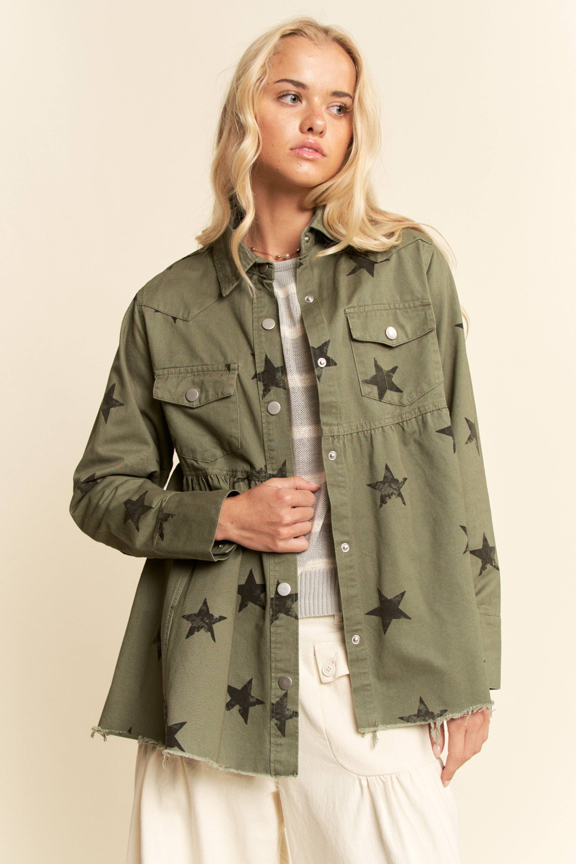 Olive star-print babydoll shacket with snap-button front, chest flap pockets, dropped shoulders, relaxed fit, and frayed curved hem.