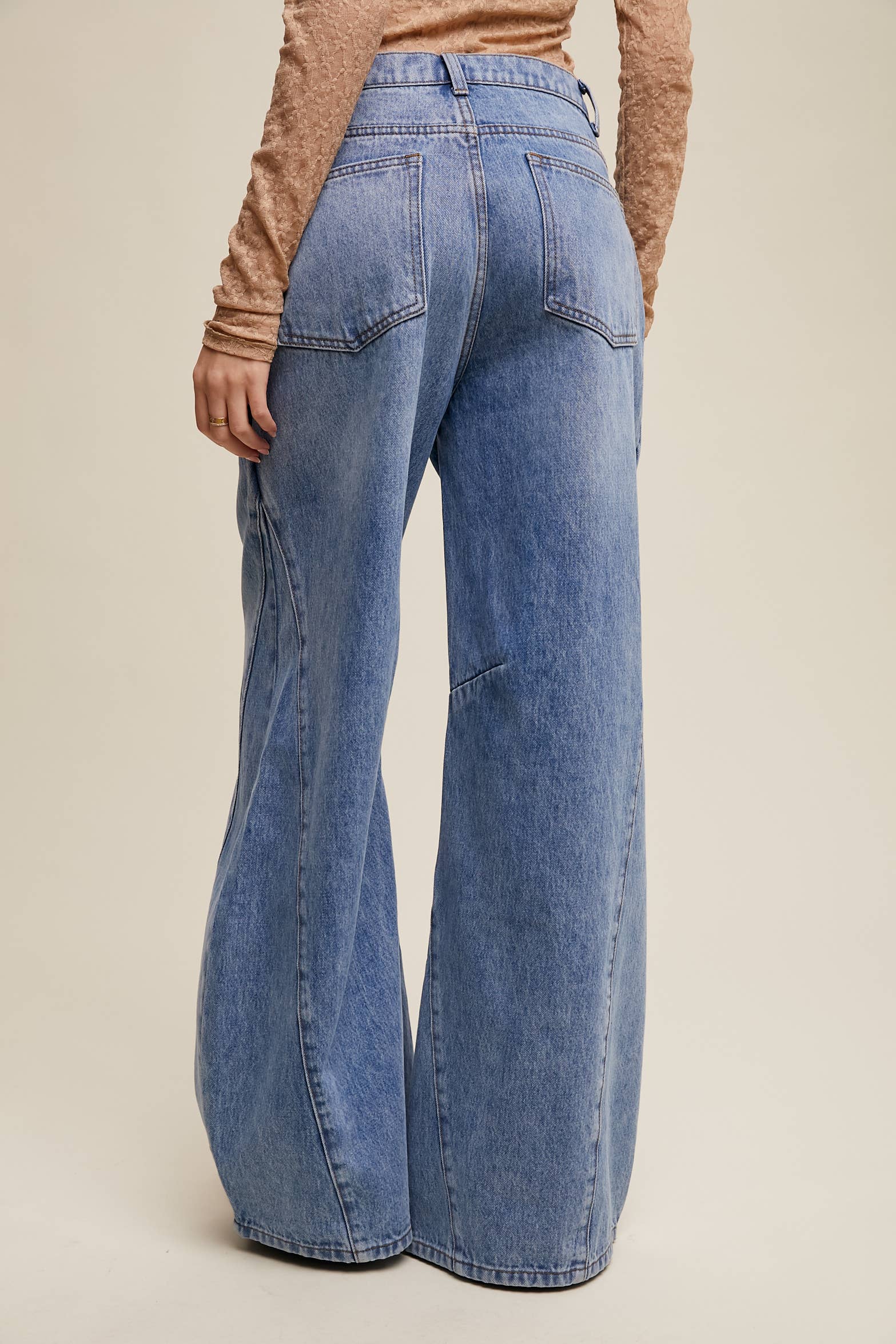 Back view- High-rise light-wash wide-leg jeans with front seam panels and knee darts, five-pocket style with zip fly, styled with tan long-sleeve top and pointed-toe boots.