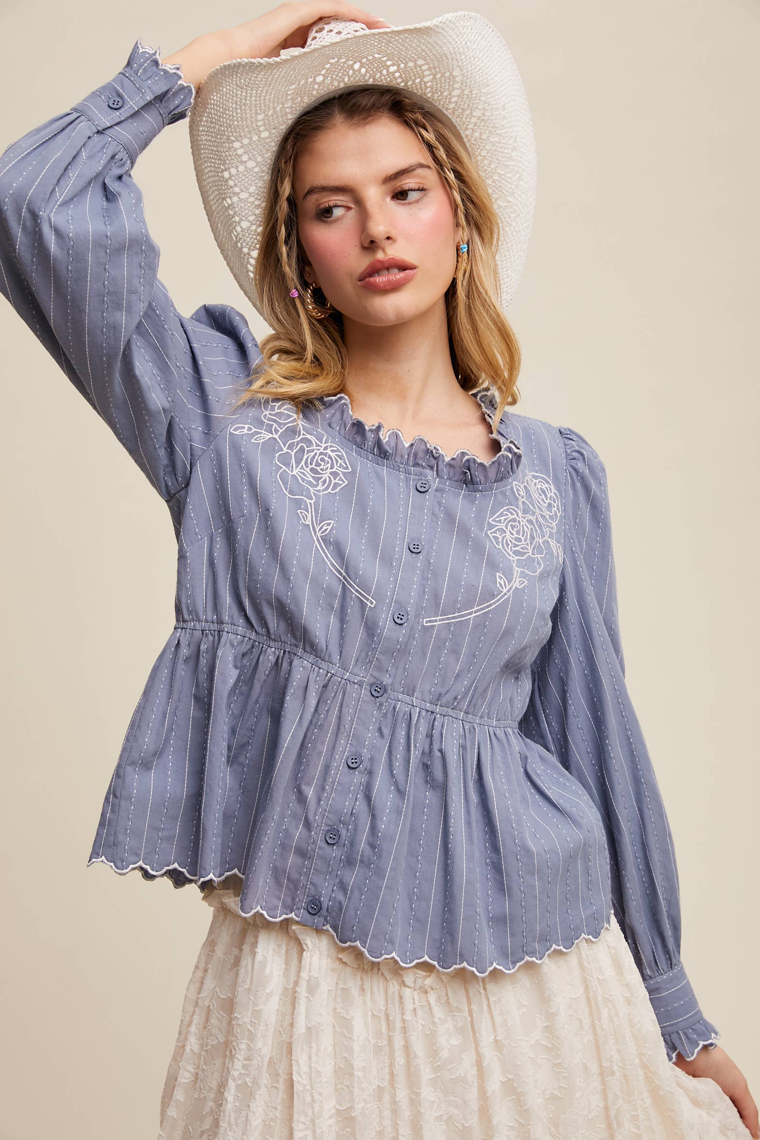 Dusty blue pinstripe blouse with ruffled neckline, white rose embroidery, puff long sleeves, button front, and scalloped peplum hem—styled with a white lace skirt and cowboy hat.