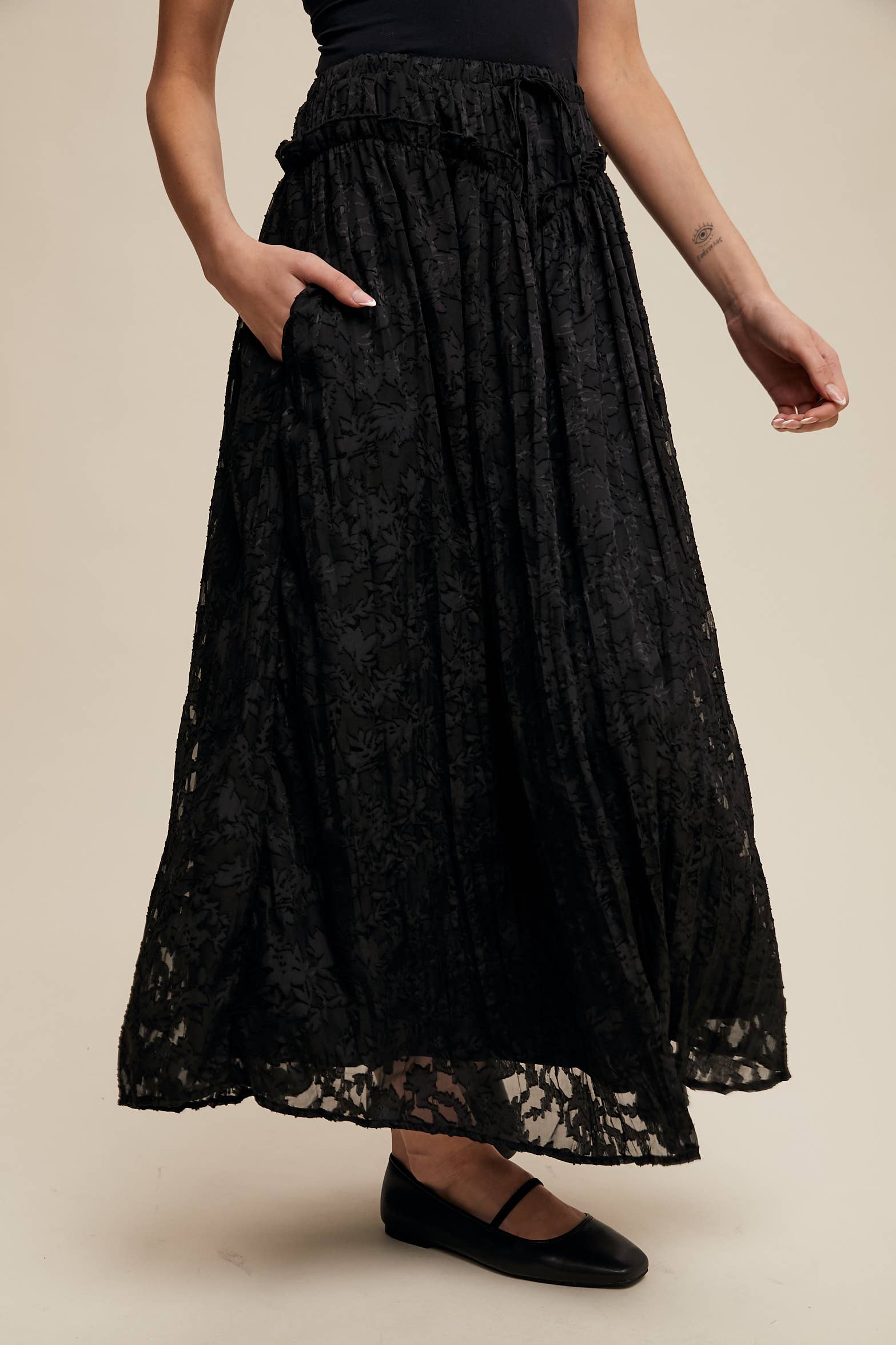 Black floral lace maxi skirt with elastic drawstring waist, ruffle trim and pockets; semi-sheer bubble hem, styled with black Mary Jane flats.