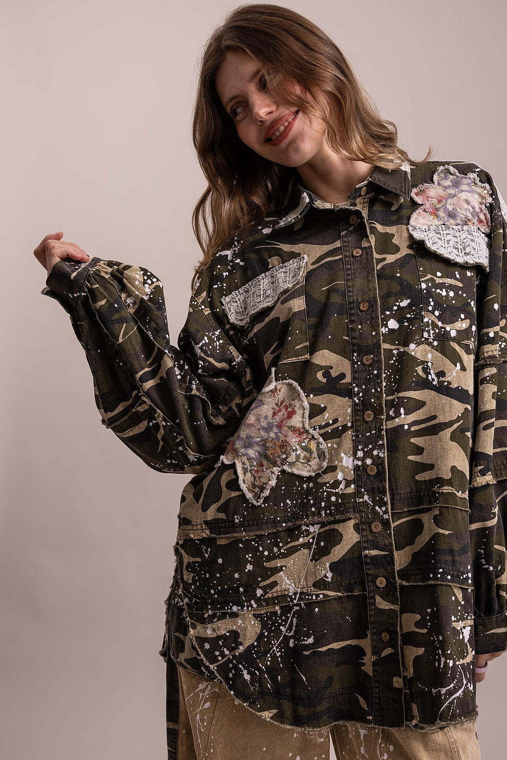 BlueVelevet camo jacket with one sleeve extended, showing patchwork seams, floral appliques and button-front closure.