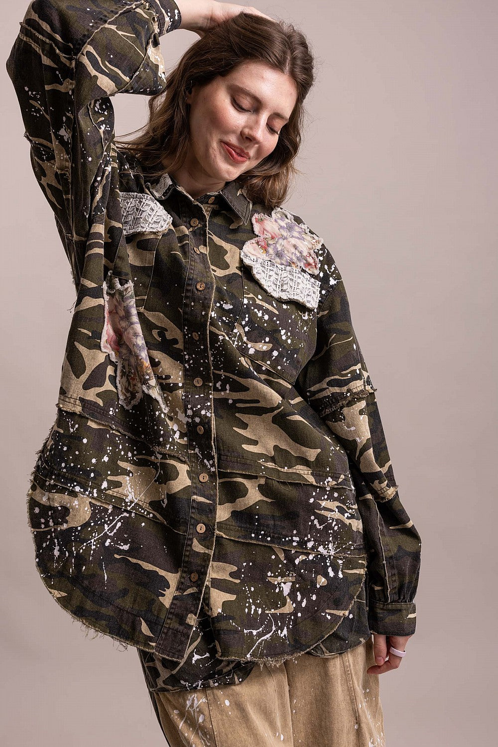 BlueVelevet Off the Trail camo patchwork jacket, arm-raised view showing white splatter detailing and a curved raw-edge hem.