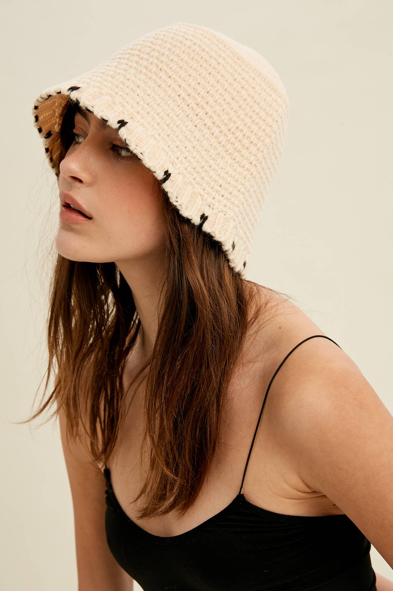 Close-up — cream knit bucket hat with contrast black whipstitch edging and soft brim, on model.