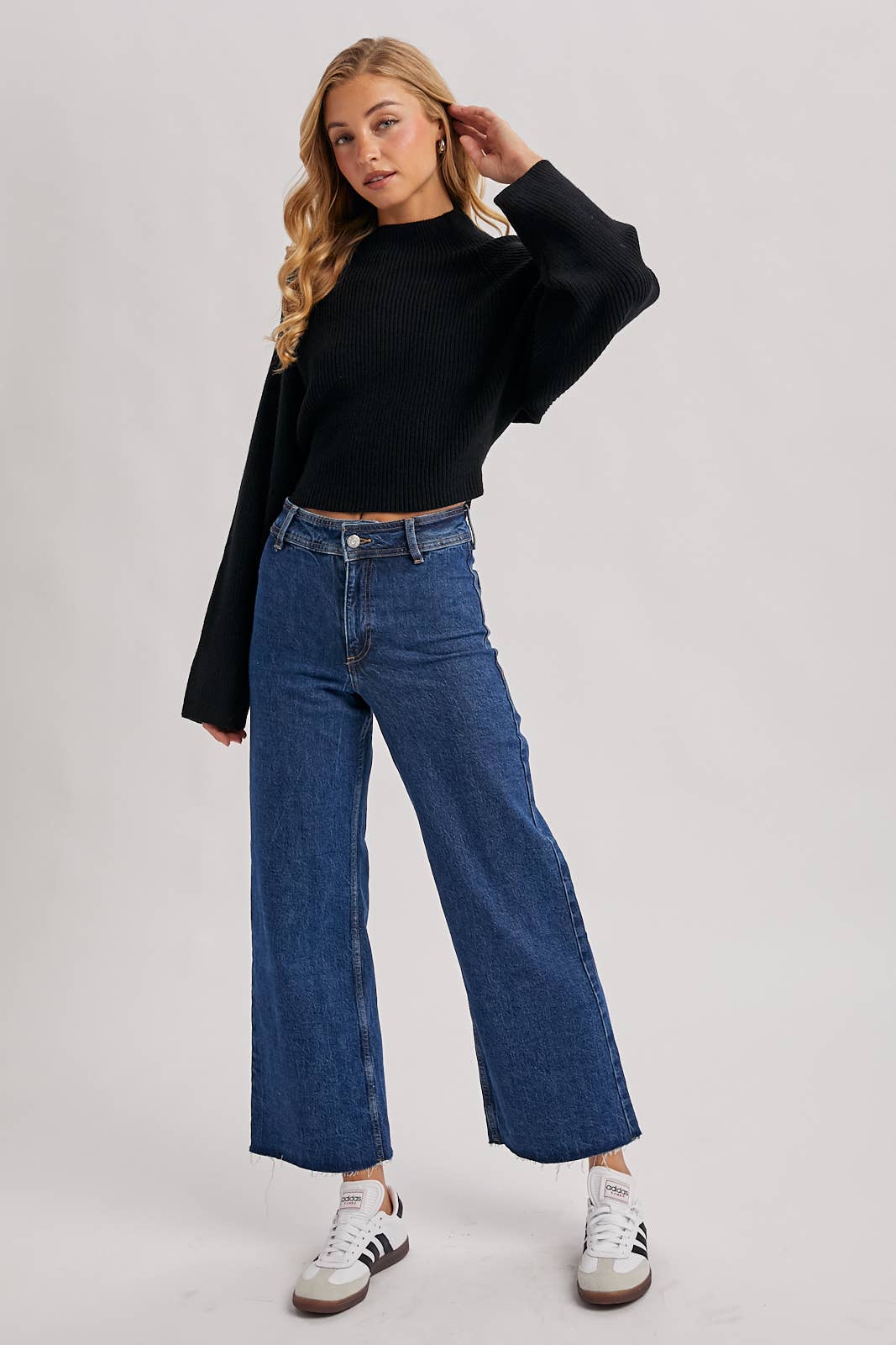 Black ribbed mock-neck sweater with long wide sleeves and a cropped fit, styled with high-rise blue jeans.