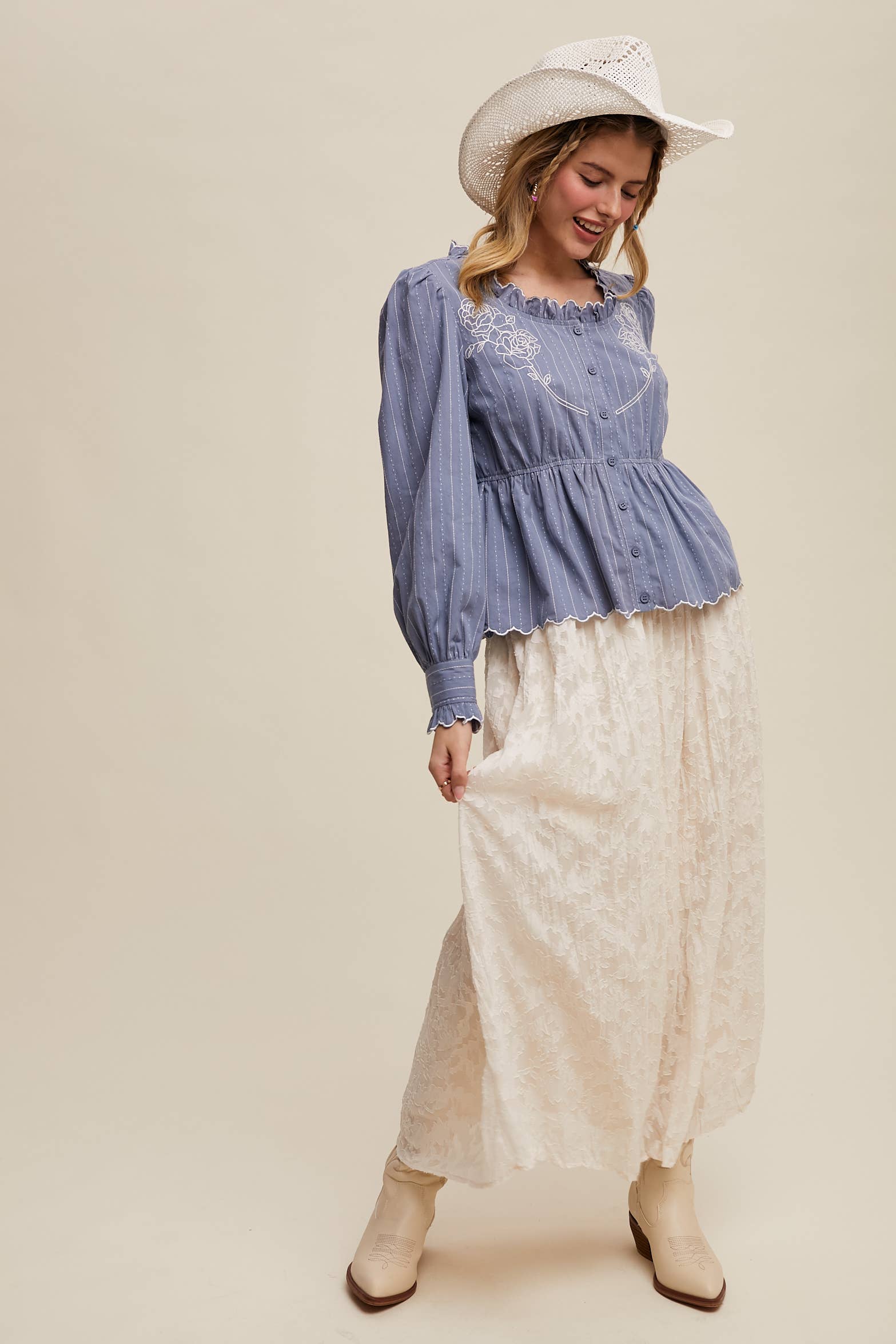 Dusty blue pinstripe blouse with ruffled neckline, white rose embroidery, puff long sleeves, button front, and scalloped peplum hem—styled with a white lace skirt and cowboy hat.