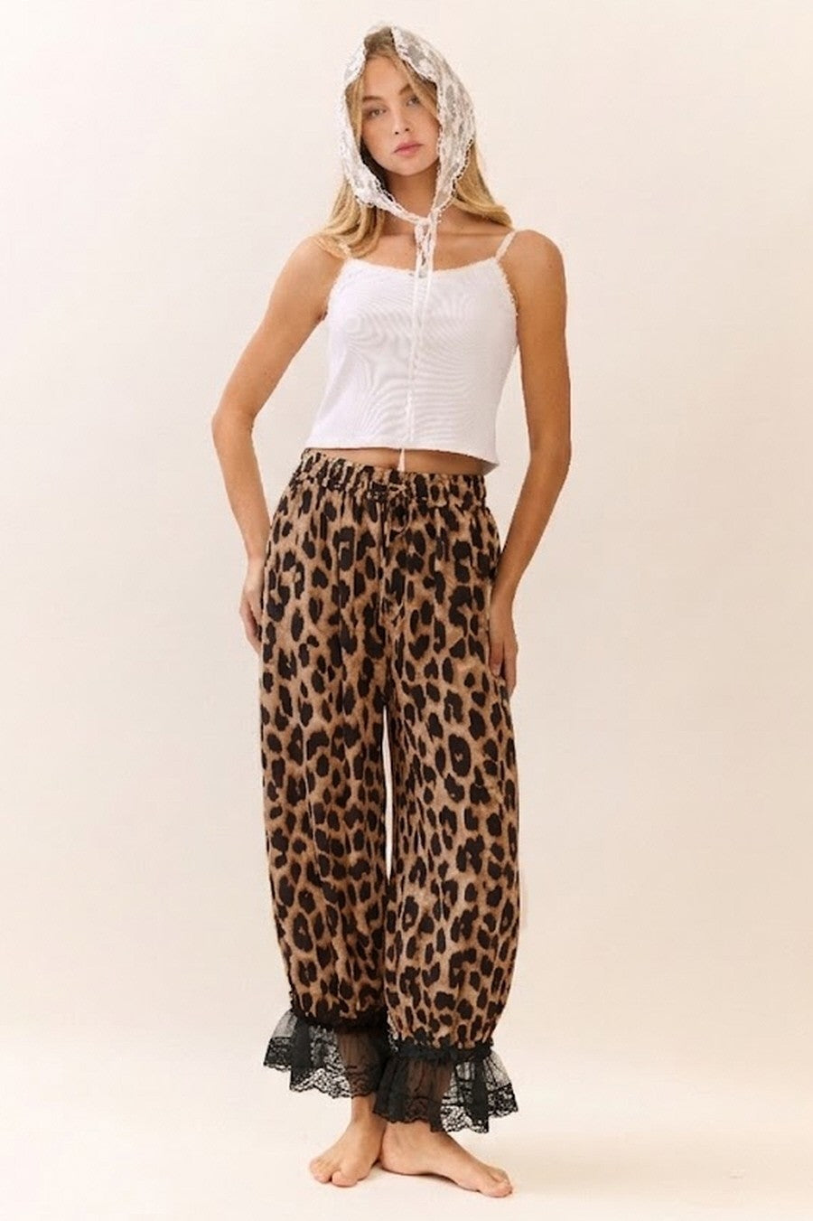 Woman wearing a white sleeveless top and leopard print pants with lace trim on a beige background