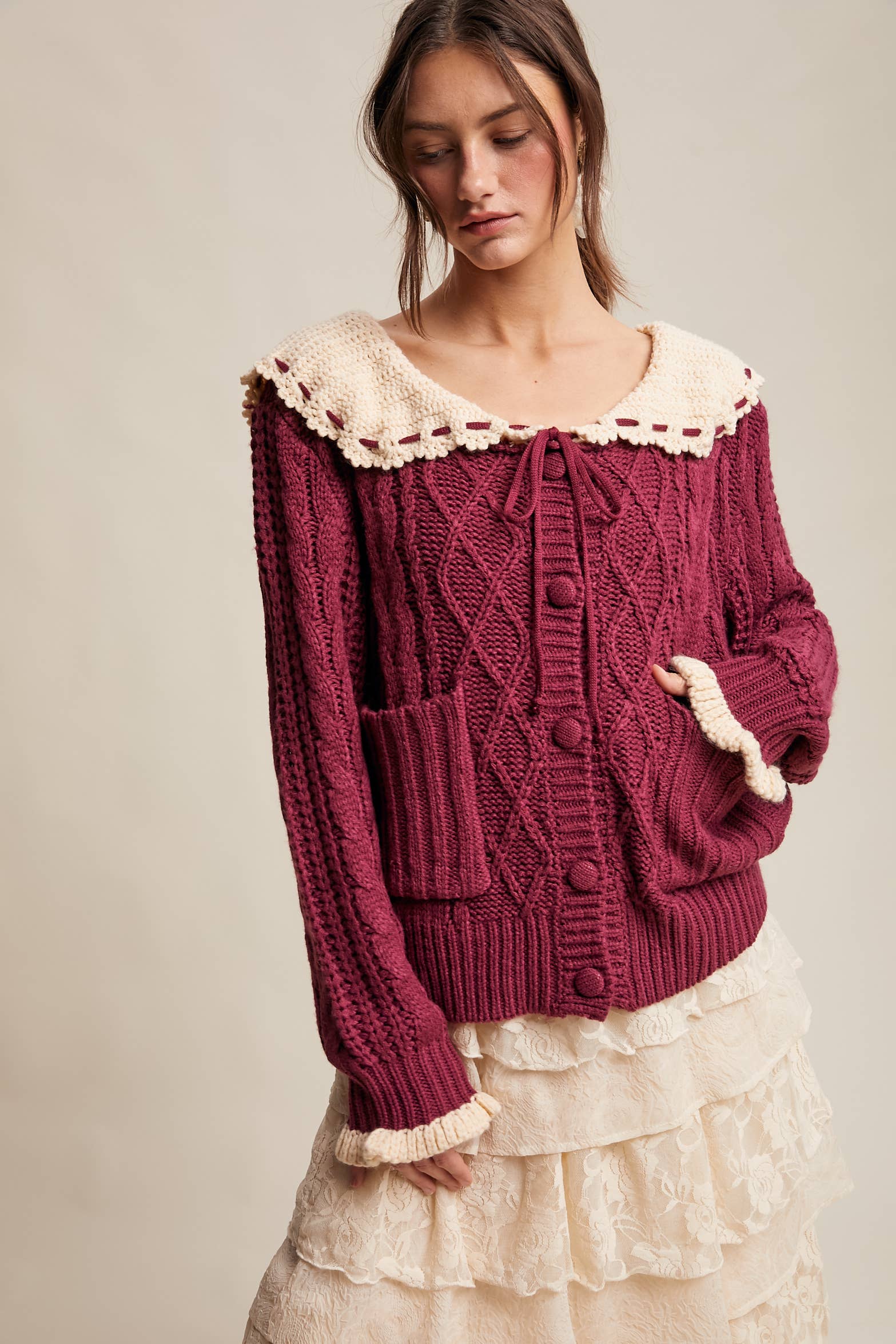 Woman wearing a burgundy knitted cardigan with lace trim on a plain background