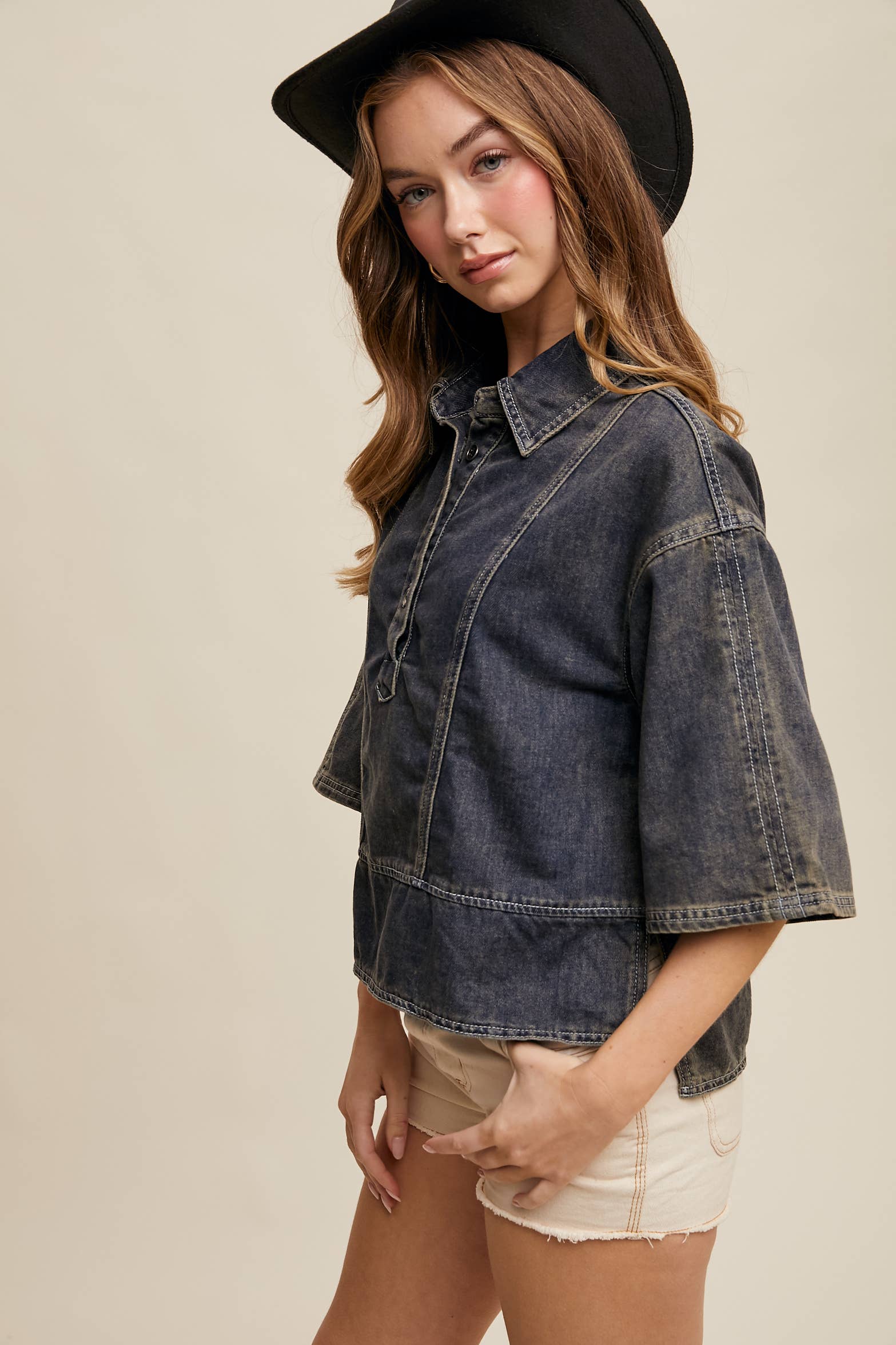 Side view- Dark-wash denim pullover top with half-button placket, exposed seam panels, and wide elbow-length sleeves in a relaxed, boxy fit.