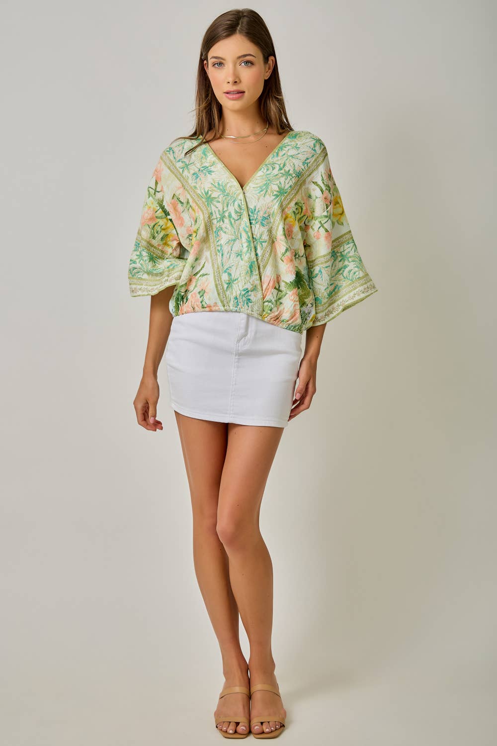 Woman wearing a floral blouse and white skirt on a plain background