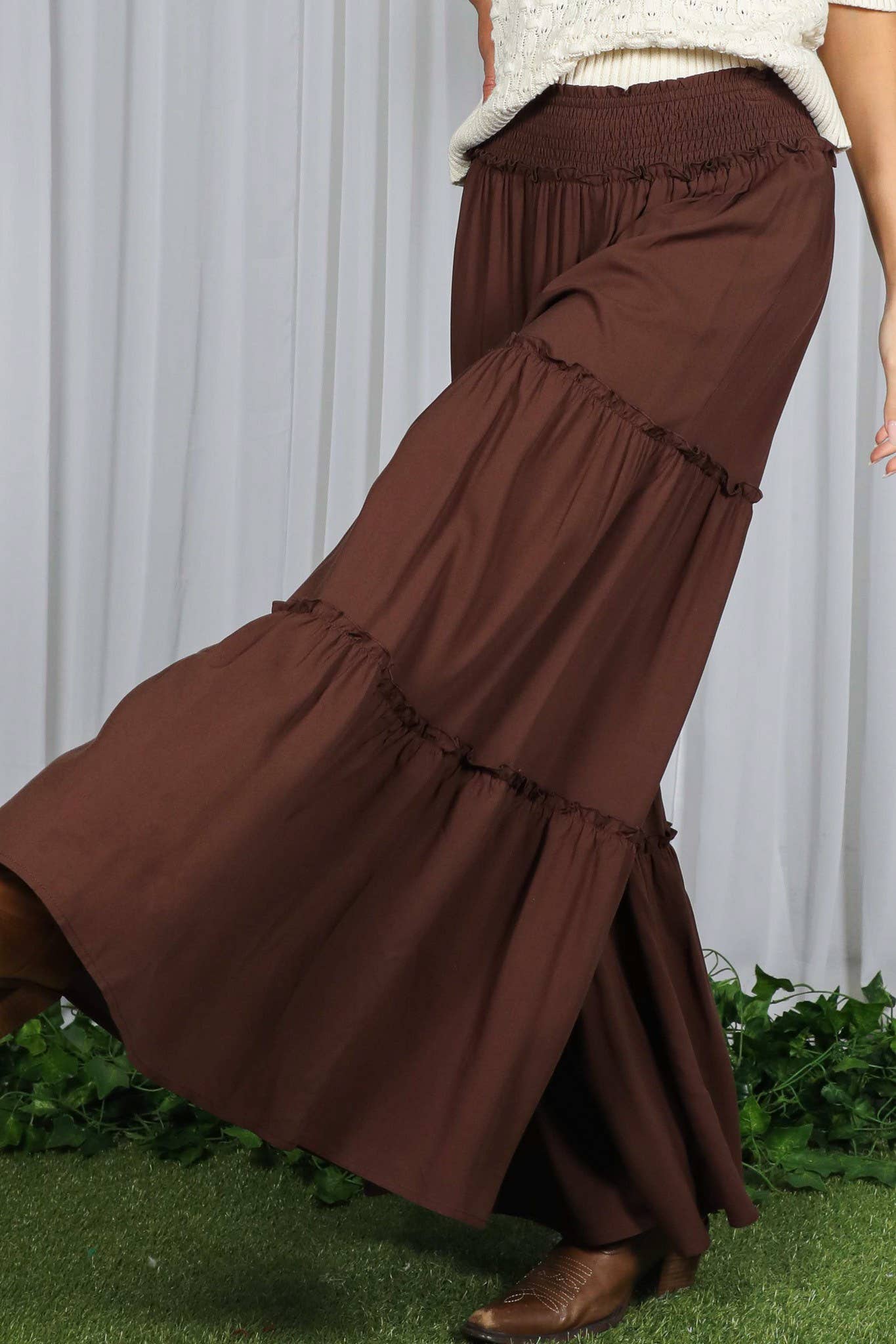 Woman wearing tiered palazzo pants with smocked waistband in mocha and black, styled for fall with sweater and boots.