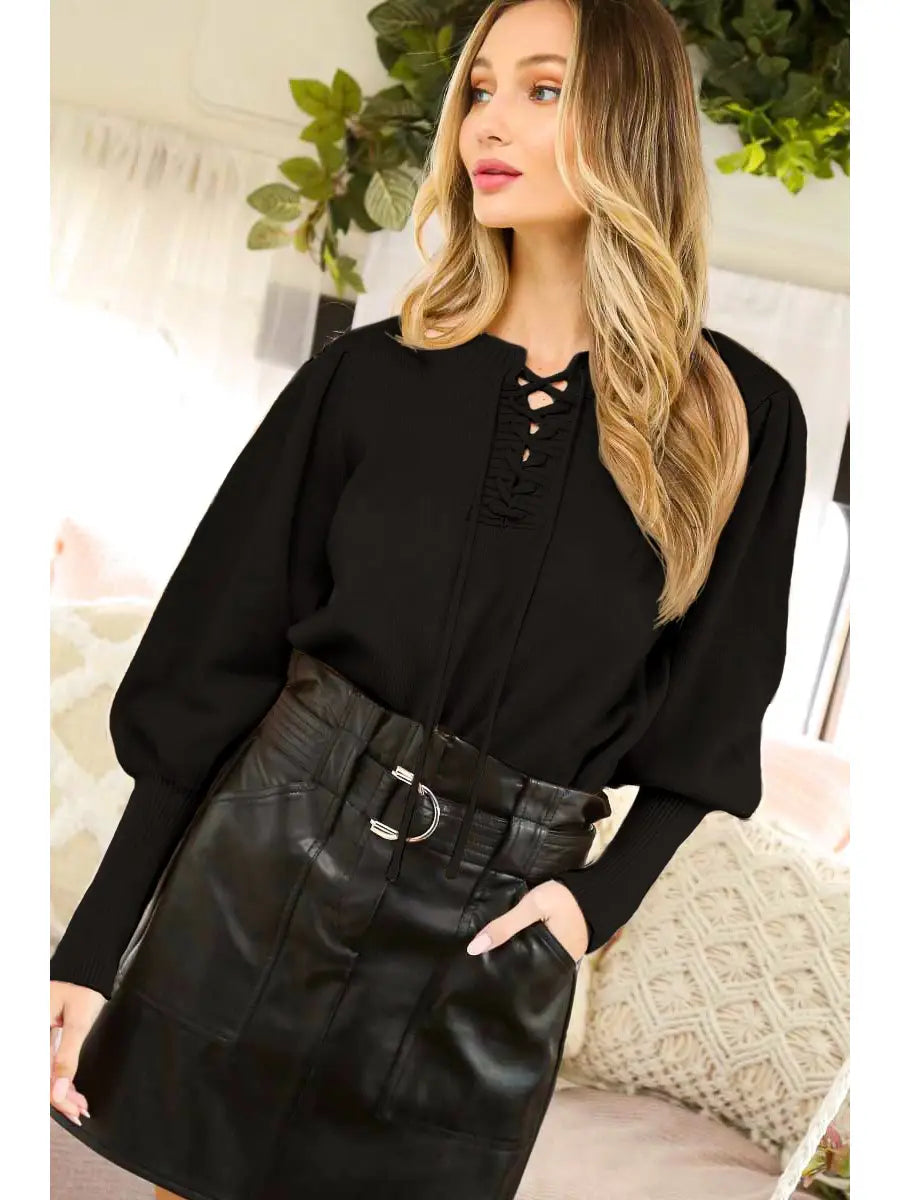 Model standing in a black lace-up V-neck sweater with long puff sleeves and fitted ribbed cuffs, tucked into a belted black mini skirt.