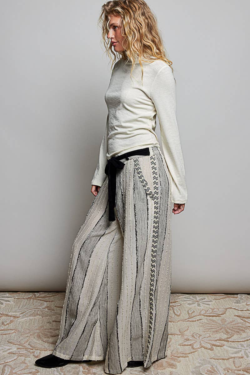 Woman wearing a light-colored top and patterned pants against a plain background