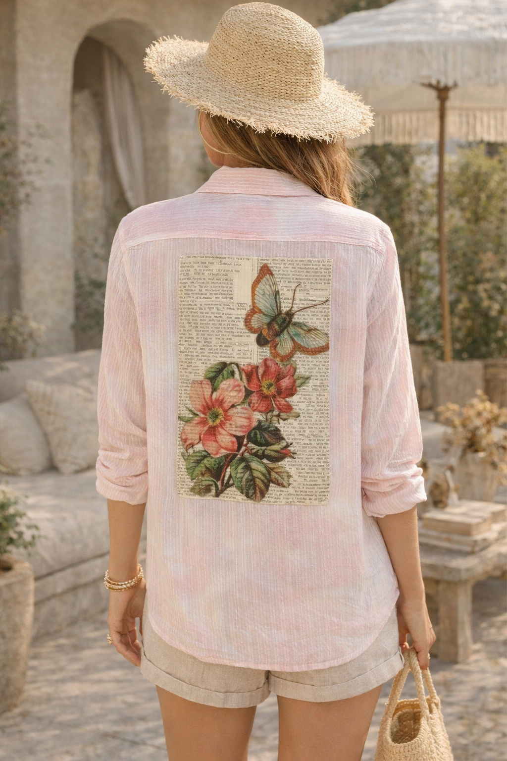 Woman wearing a light pink shirt with a butterfly and floral design outdoors.