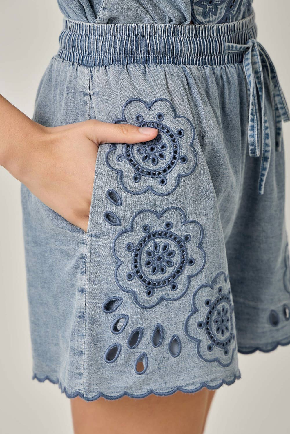 Close up view with model showing pockets Eyelet Embroidered Washed Tencel Shorts in Dark Denim — scallop hem, drawstring waist, and boho eyelet detail