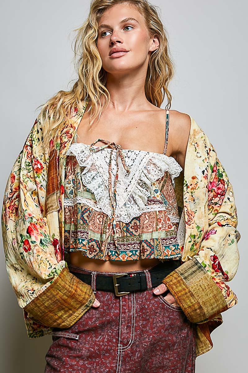 Peace in Bloom Yellow Floral Reversible Boho Jacket a colorful floral jacket over a patterned top and maroon pants on a plain background